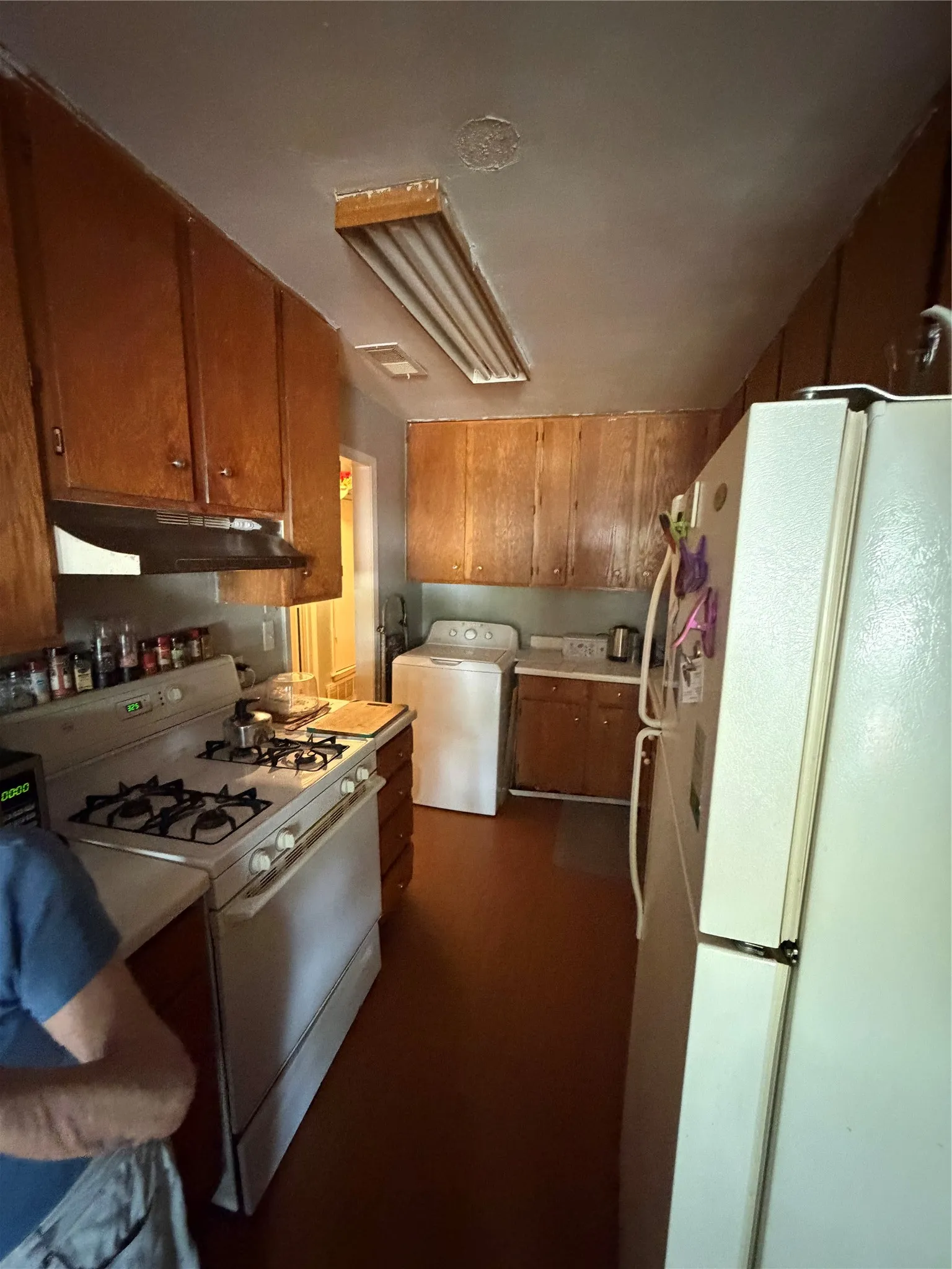 Galley kitchen featuring wood cabinetry, white countertops, a gas range, and a washer/dryer unit