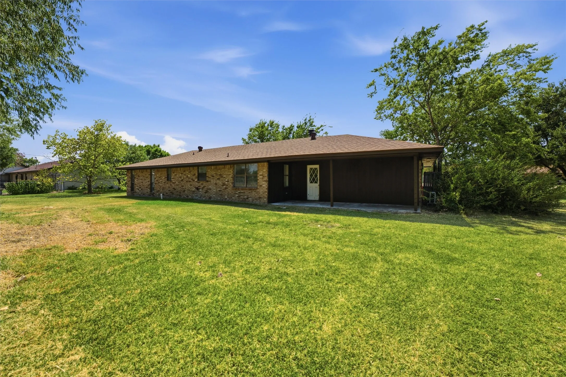 Expansive backyard featuring a manicured lawn, mature trees, and a covered patio