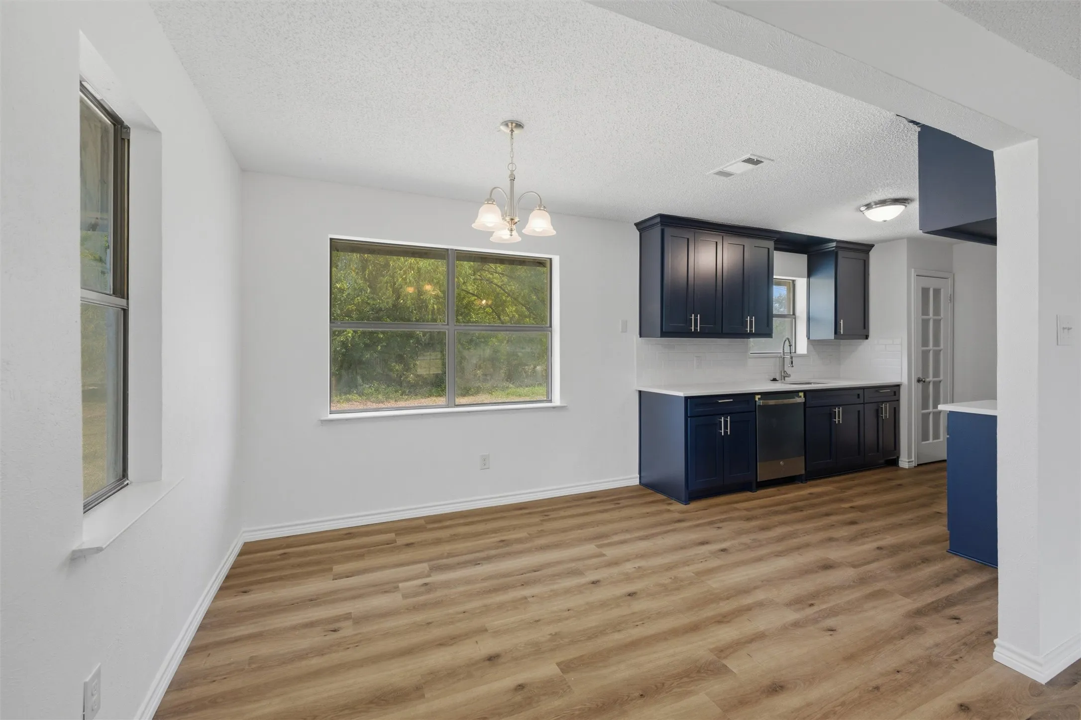 Open-concept kitchen and dining area featuring wood-finish flooring, white walls, and a window for natural light