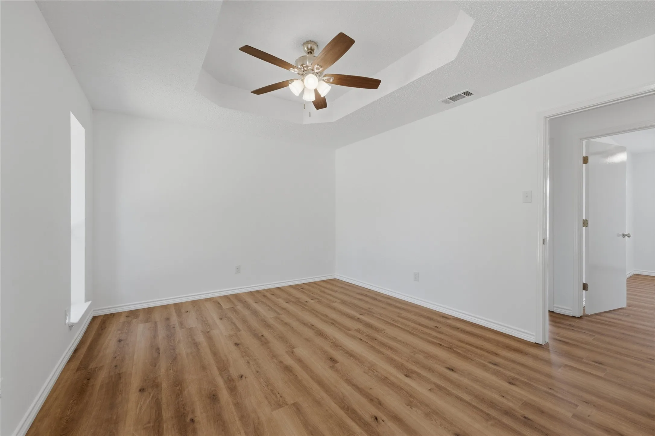 Spacious interior room featuring wood-finish flooring, a tray ceiling, and a ceiling fan with integrated lighting