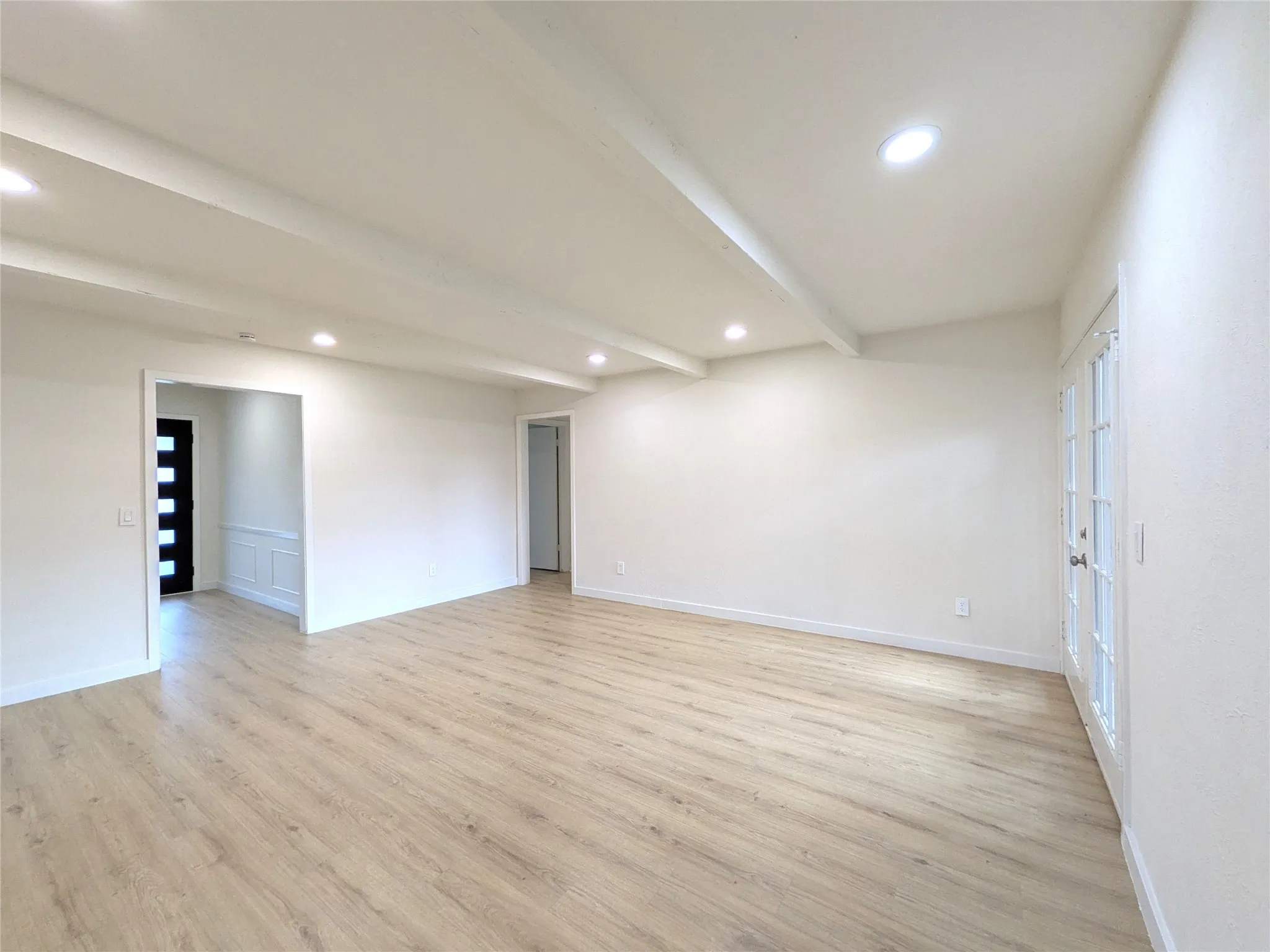 Spacious living area featuring light wood-finish flooring, recessed lighting, and exposed ceiling beams