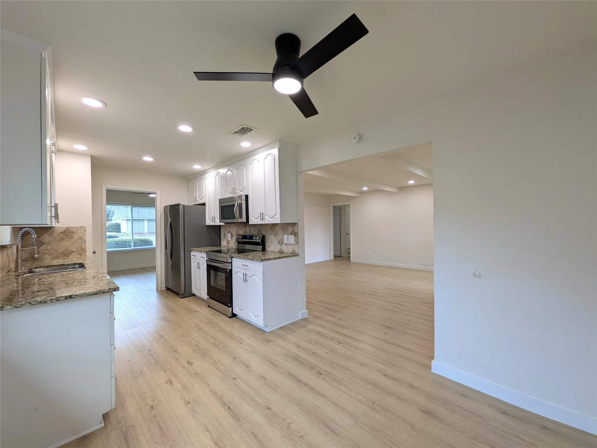 Kitchen featuring wood-finish flooring, white cabinetry, granite countertops, stainless steel appliances, and a tiled backsplash