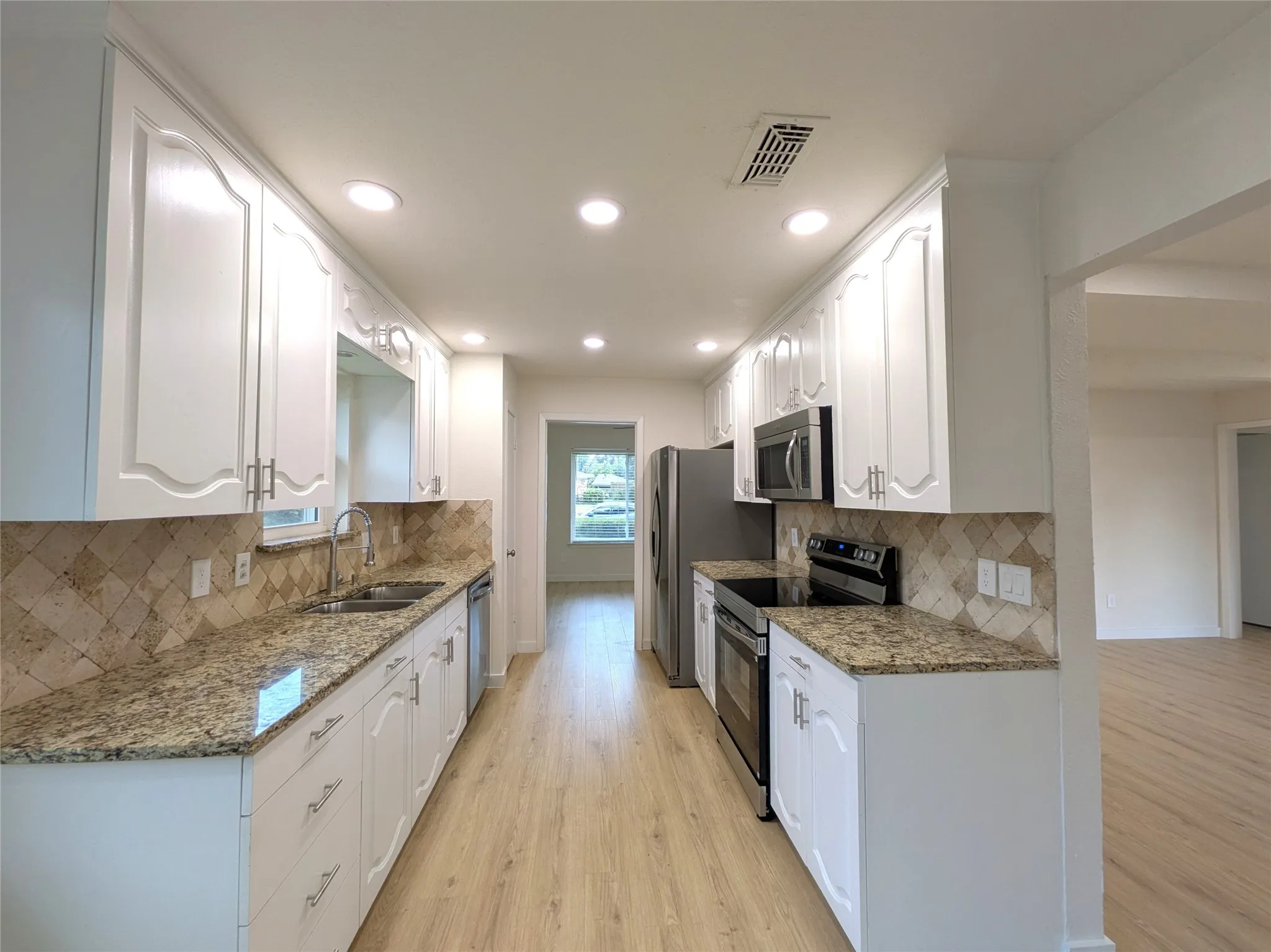 Galley kitchen featuring white cabinetry, granite-finish countertops, stainless steel appliances, a tile backsplash, and wood-finish flooring