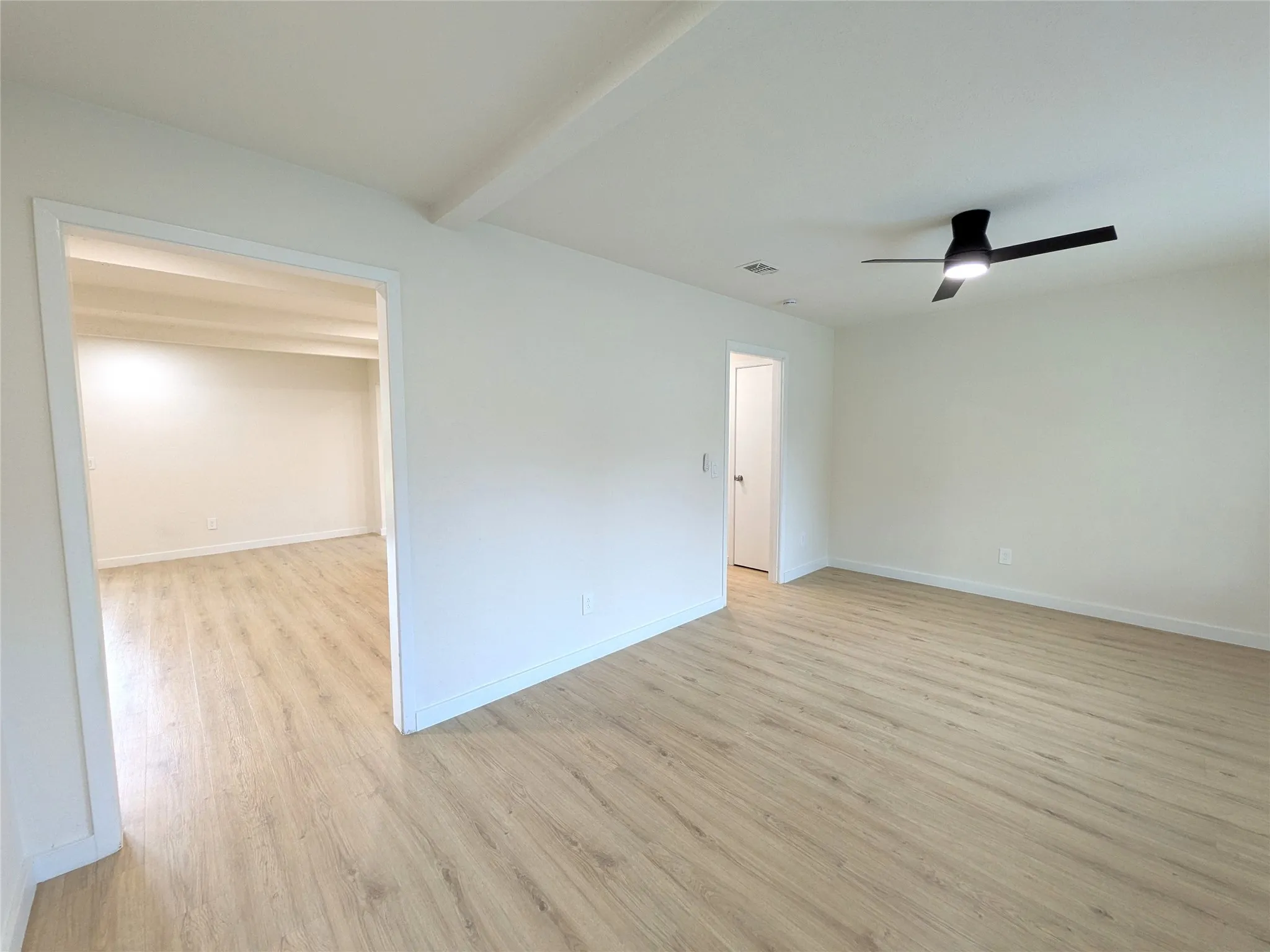 Bright interior space featuring light wood-finish flooring, white walls, and a modern black ceiling fan with integrated lighting