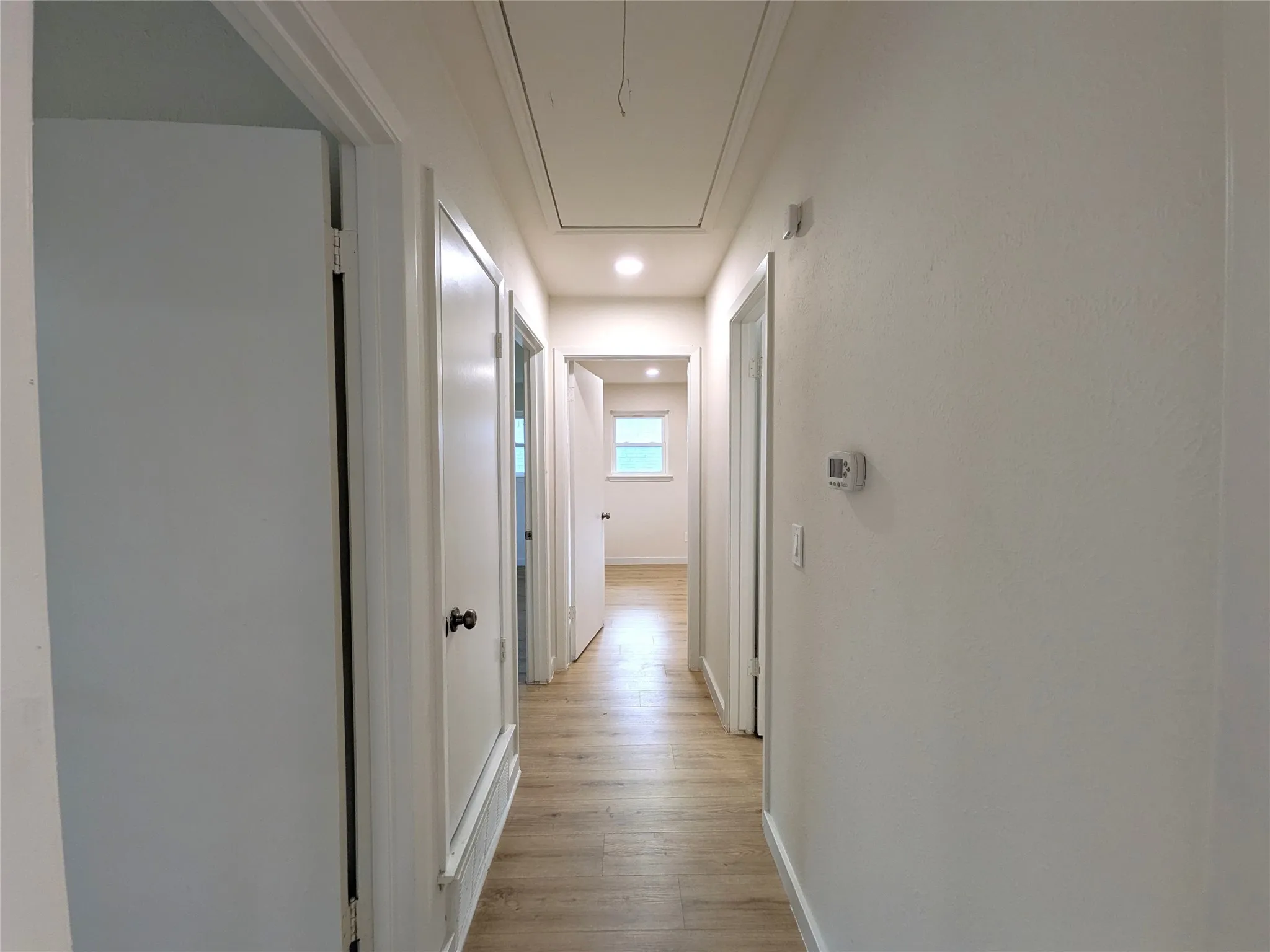 Hallway featuring wood-finish flooring, recessed lighting, white walls, and multiple panel doors