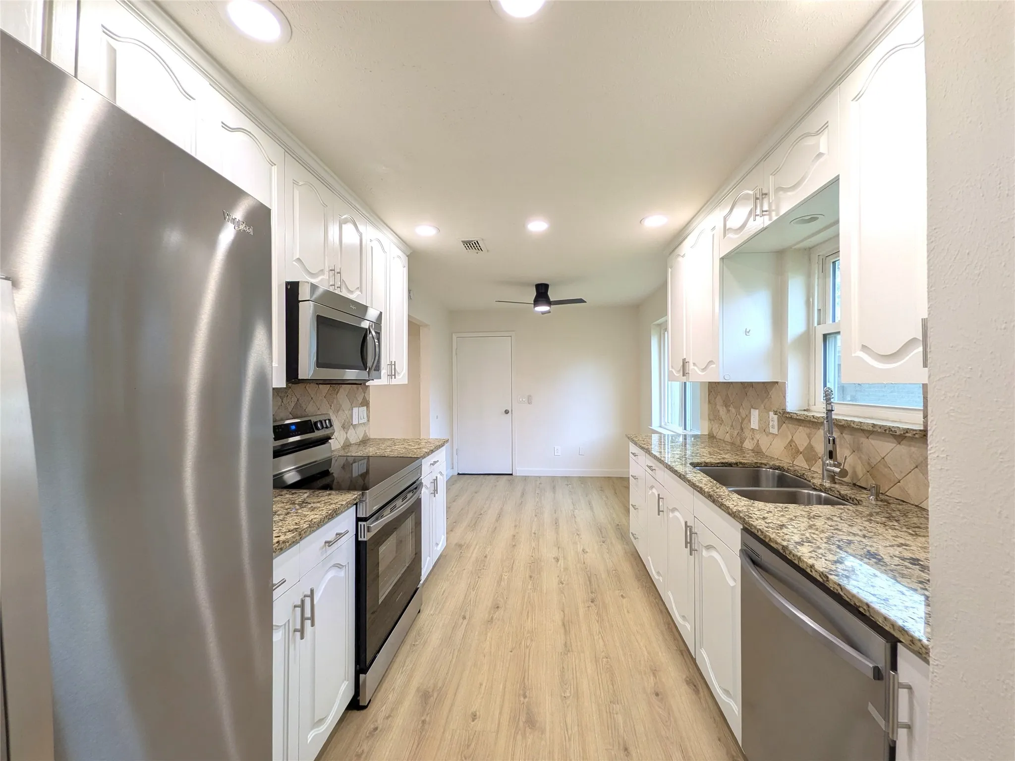 Updated kitchen featuring white cabinetry, stone countertops, stainless steel appliances, recessed lighting, and wood-finish flooring