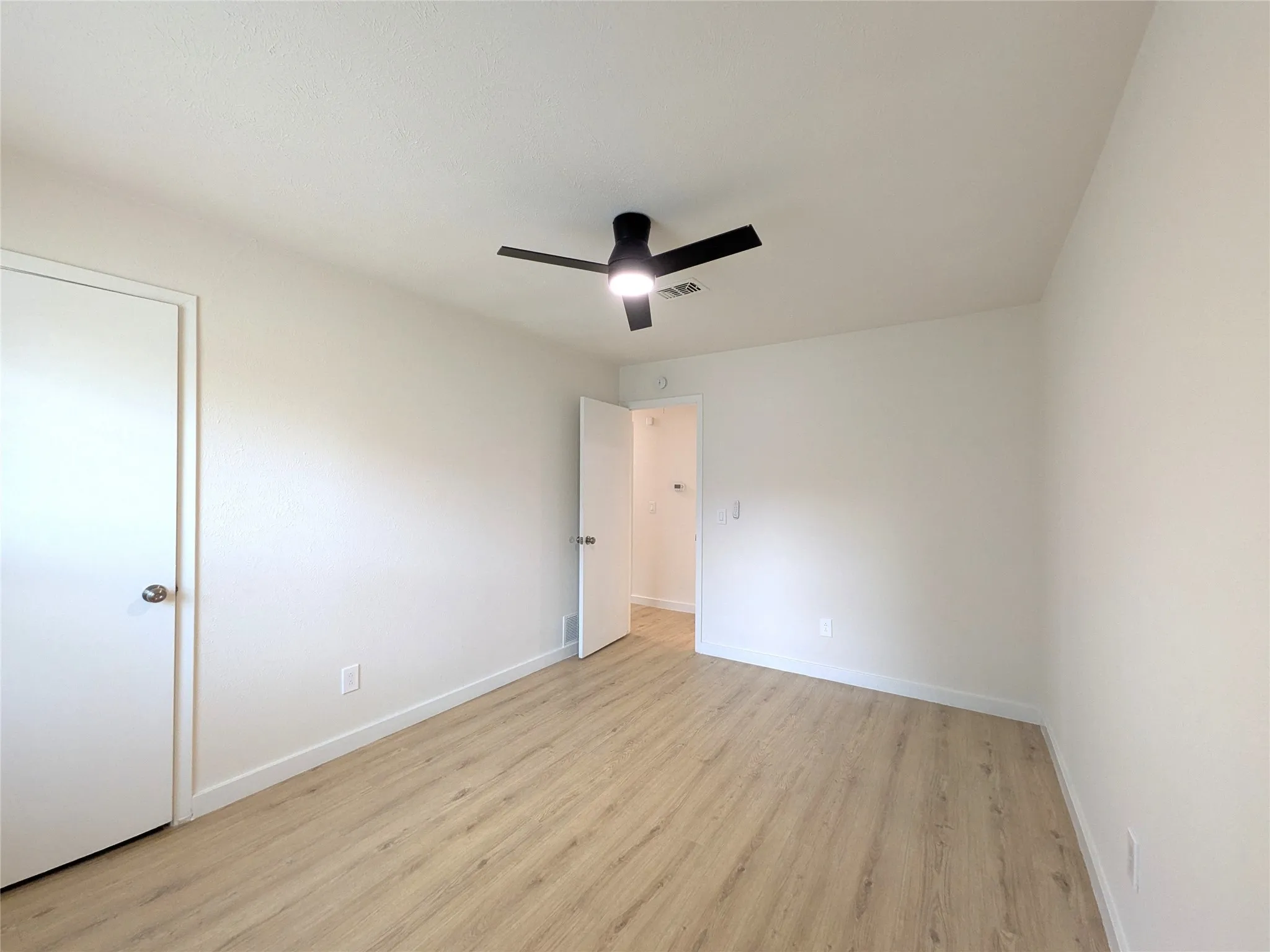 Bright interior room featuring wood-finish flooring, white walls, and a contemporary ceiling fan