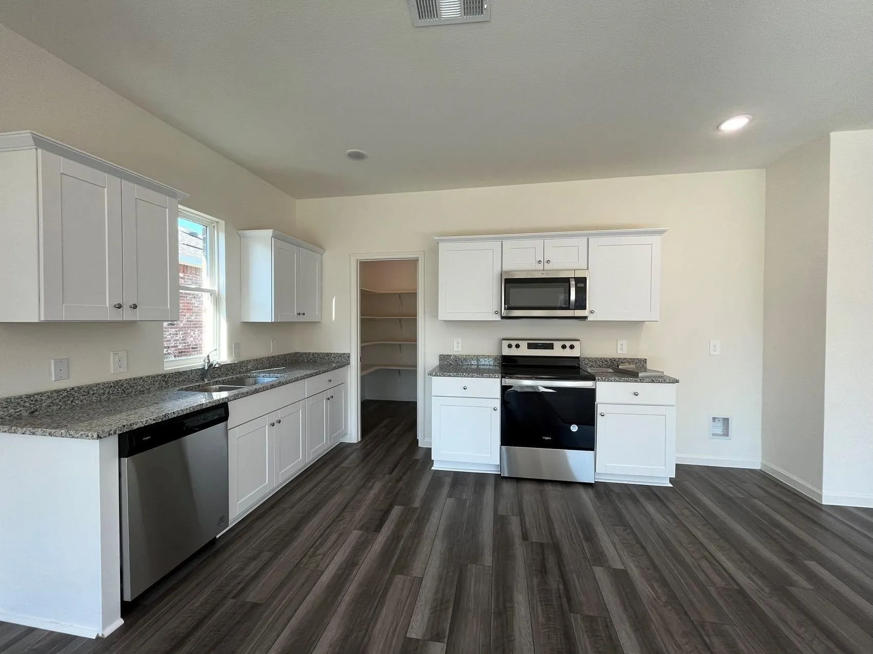 Kitchen with white cabinetry, stainless steel appliances, dark wood-style floors, dark stone countertops, and recessed lighting