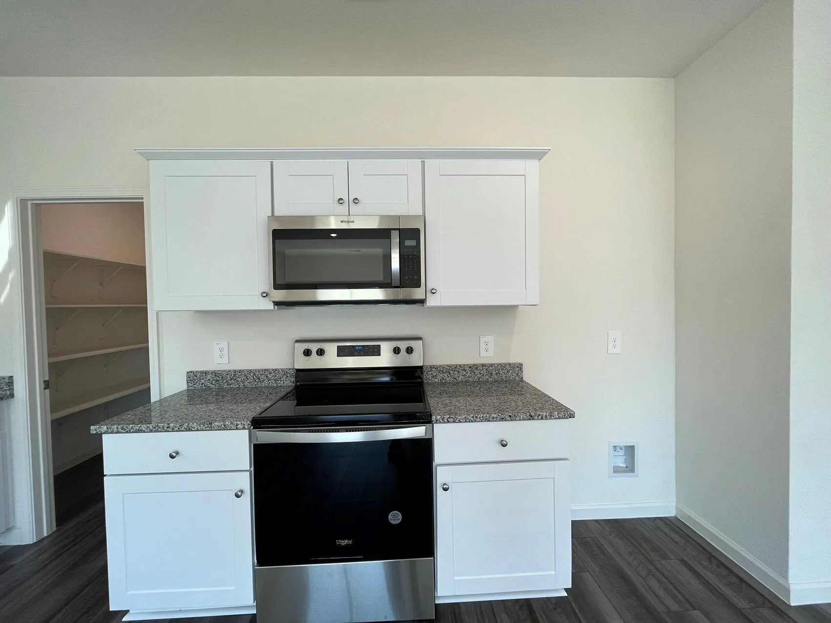 Kitchen with stainless steel appliances, white cabinets, dark wood-type flooring, and dark stone countertops