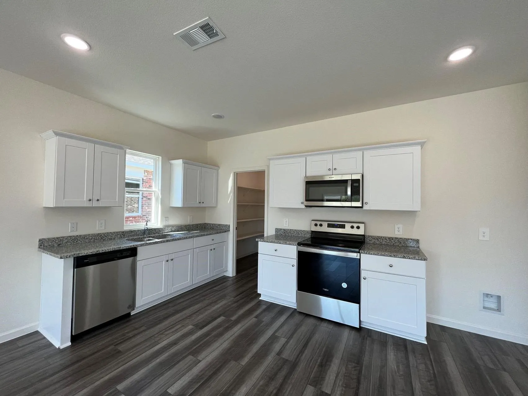 Kitchen with white cabinetry, stainless steel appliances, dark stone countertops, dark wood-style flooring, and recessed lighting