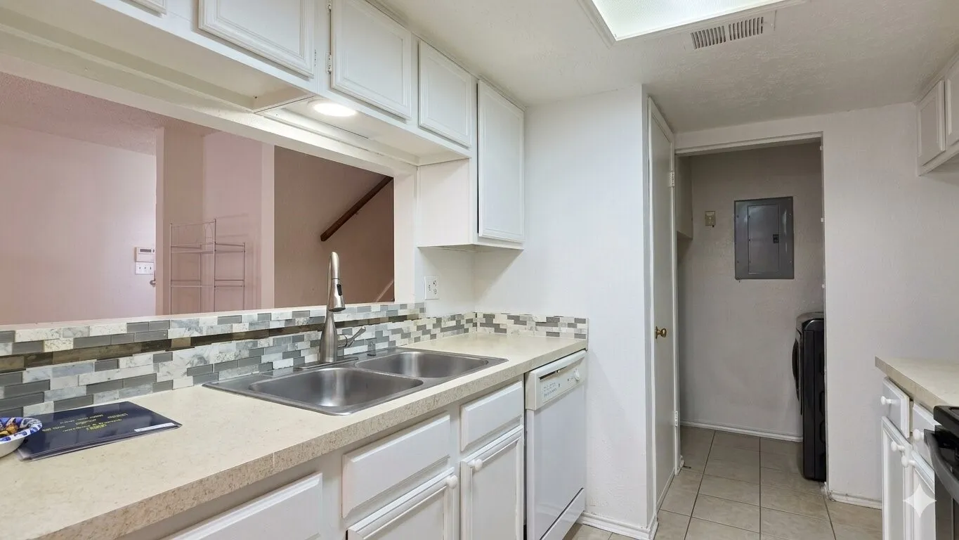 Kitchen featuring white cabinetry, light-toned countertops, a dual basin stainless steel sink with a modern faucet, and a patterned backsplash