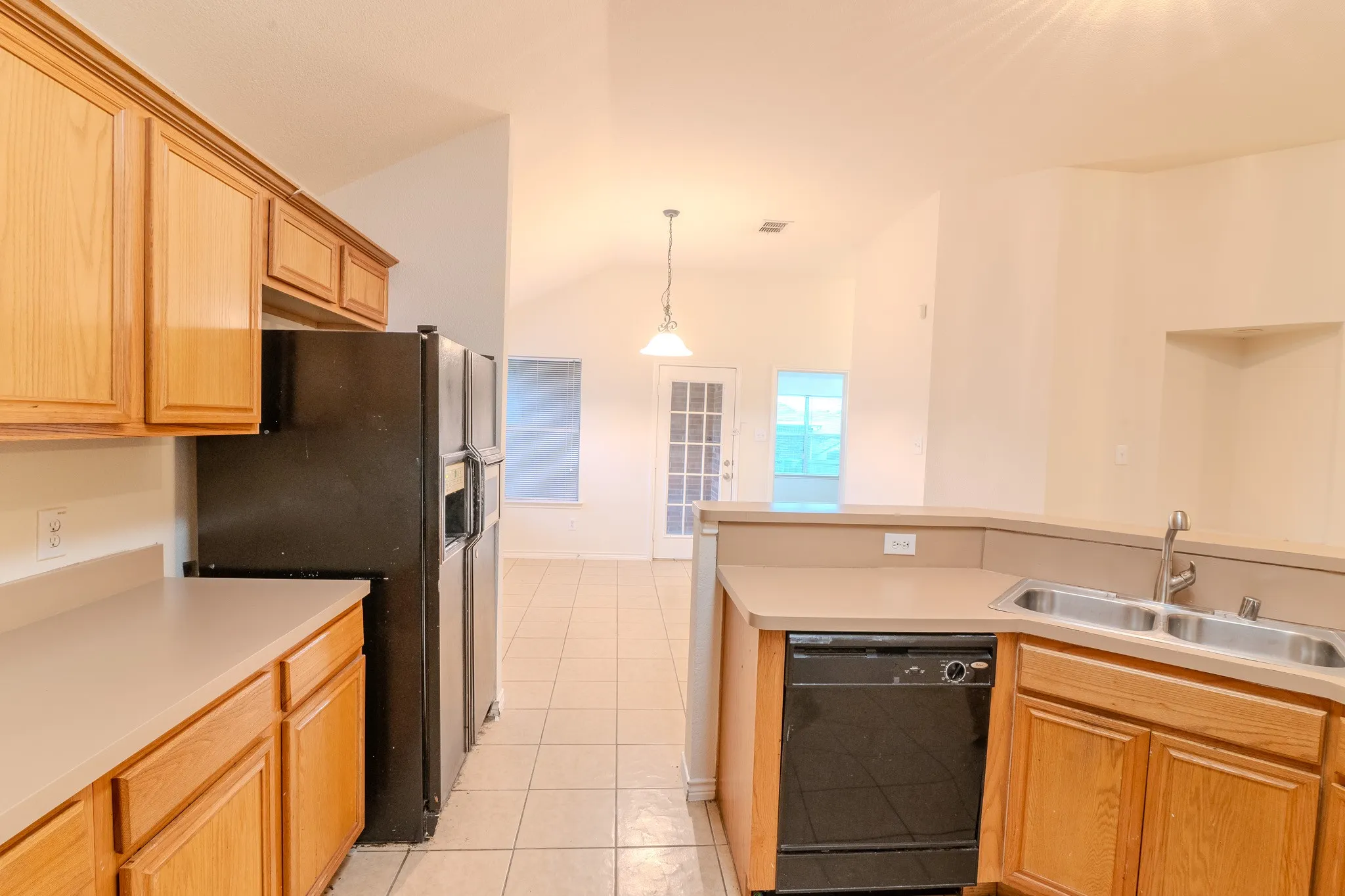 Kitchen featuring wood-finish cabinetry, light-toned countertops, a double basin sink, and a black dishwasher