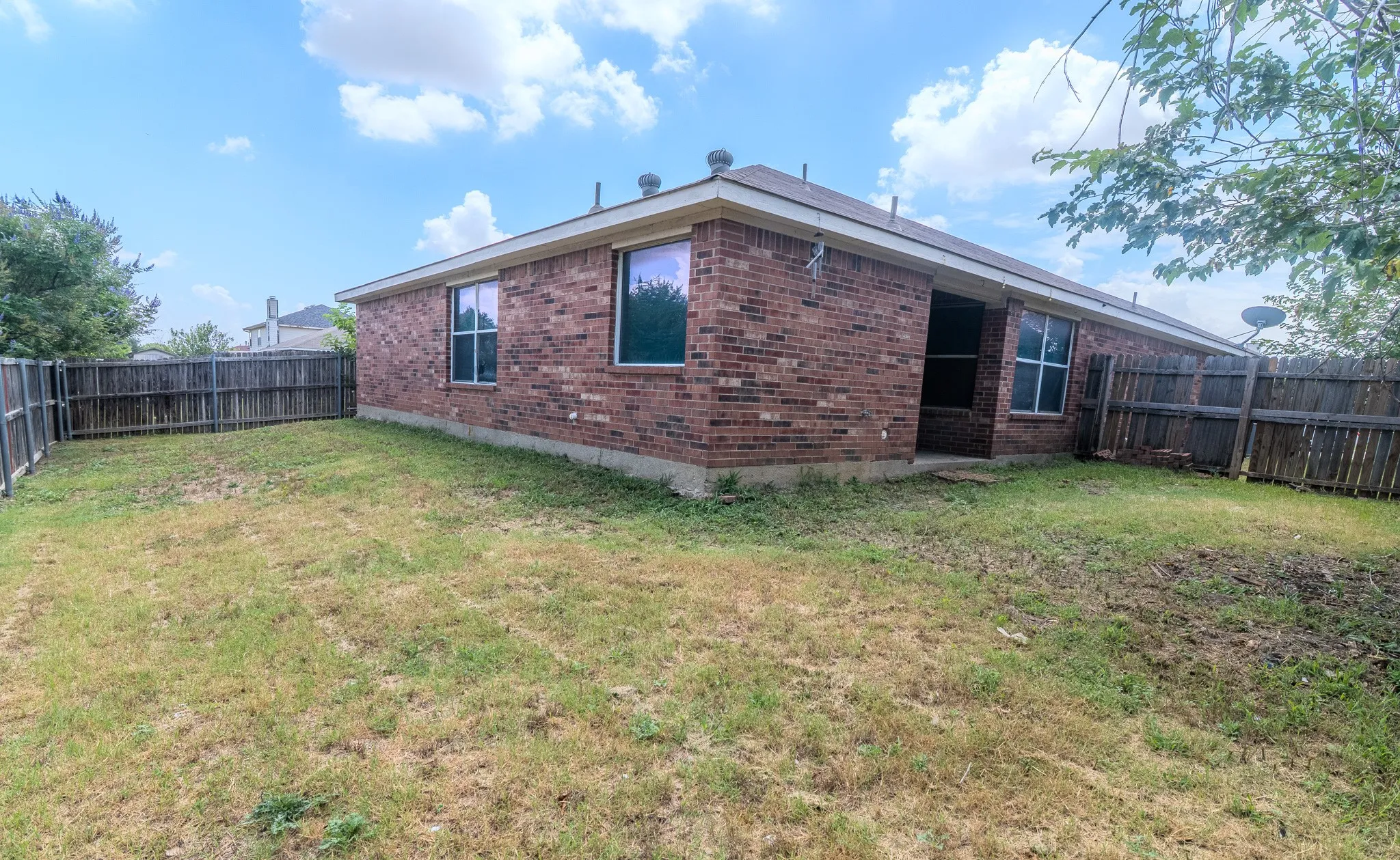 Private backyard featuring a brick exterior, perimeter fencing, multiple windows, and a rear door