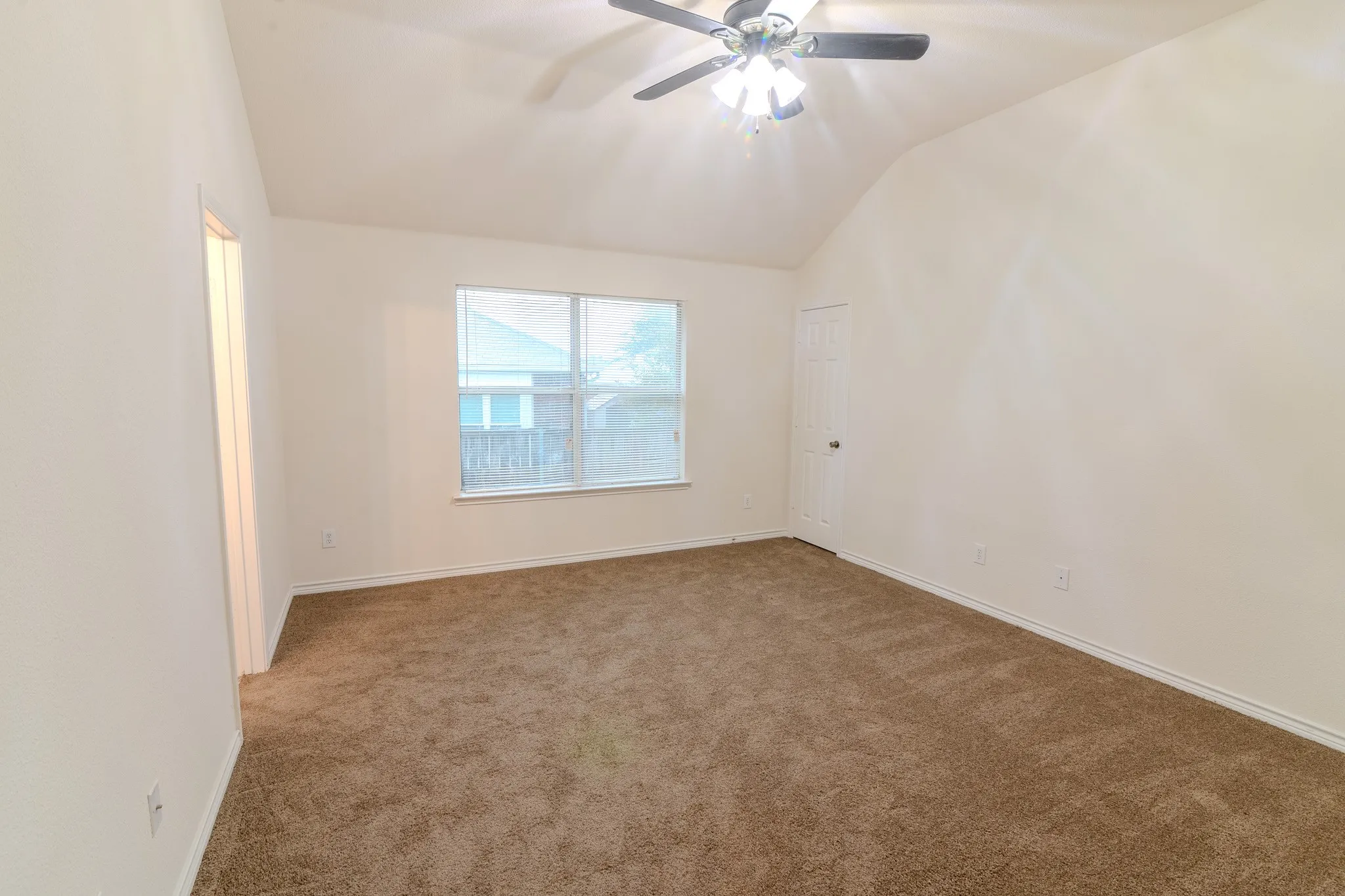 Spacious room featuring vaulted ceilings, a ceiling fan with light fixture, light brown carpeting, a window with blinds, and white walls