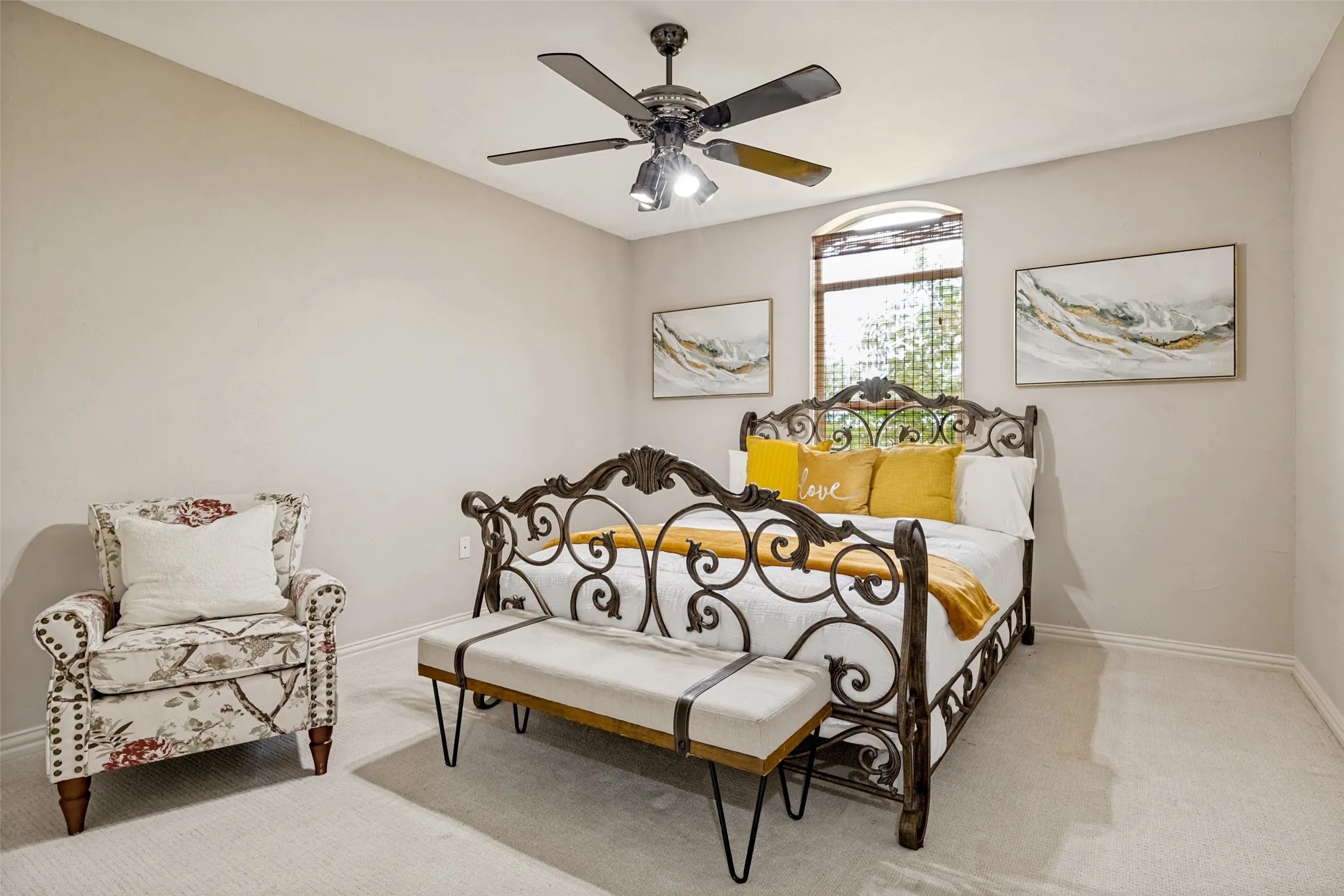 Spacious carpeted quest room featuring a ceiling fan with integrated lighting, an arched window, and neutral wall tones