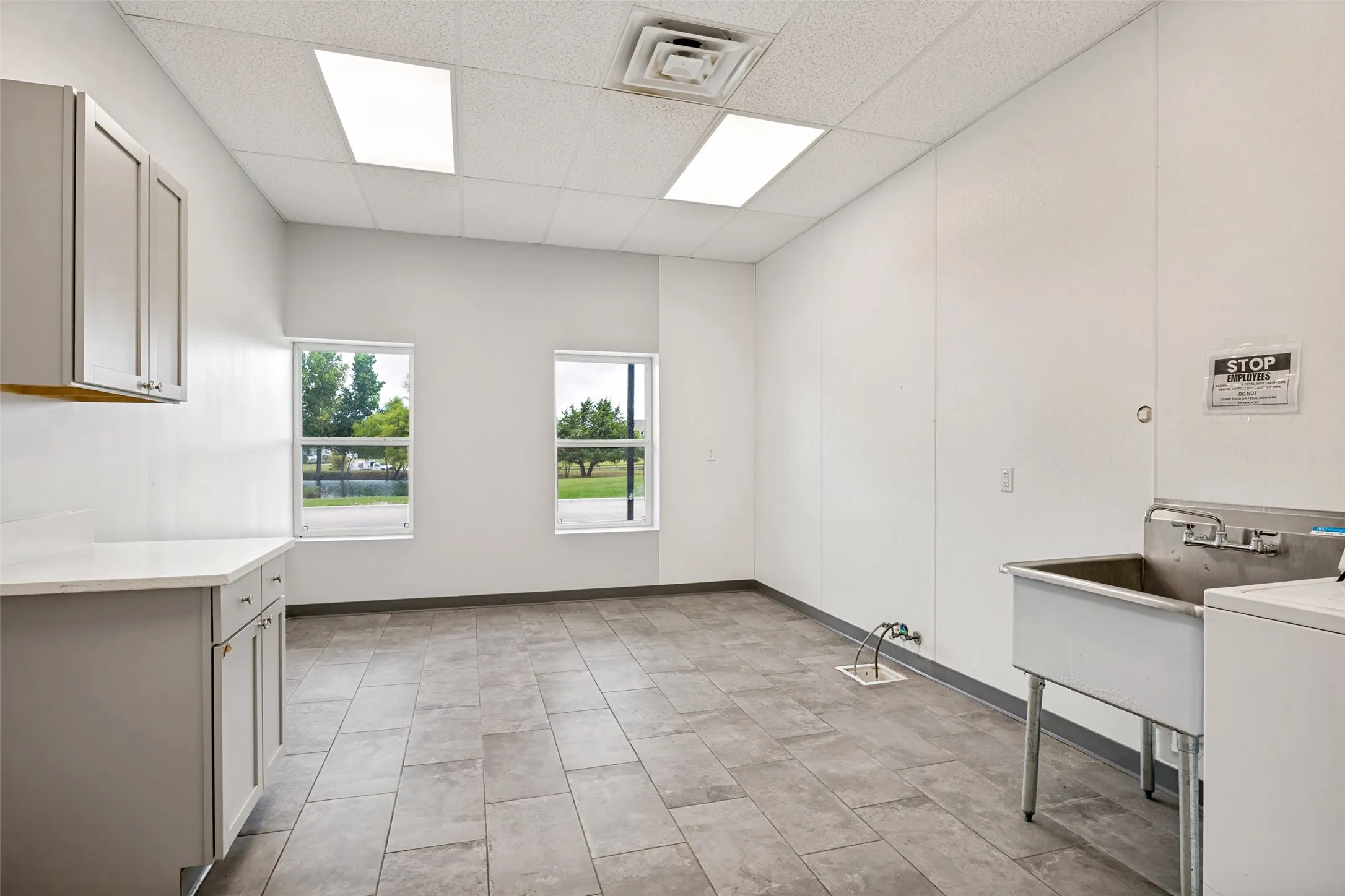 Spacious utility area featuring a large utility sink, ample cabinetry with a light countertop, and tile flooring This area was used as grooming, bathing of dogs for Kennel.