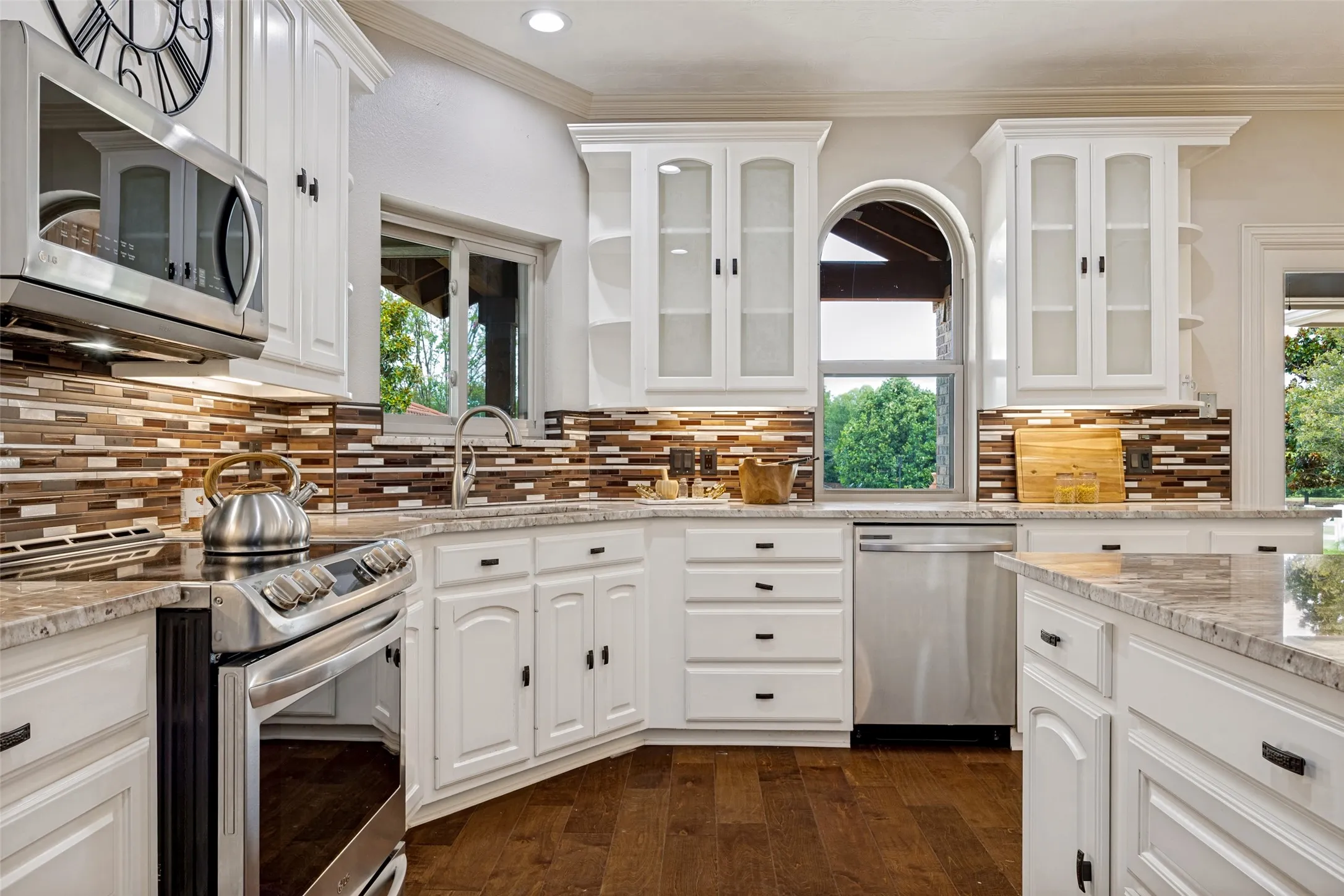 Kitchen featuring white cabinetry, stainless steel appliances, mosaic tile backsplash, wood-finish flooring, and light-toned countertops