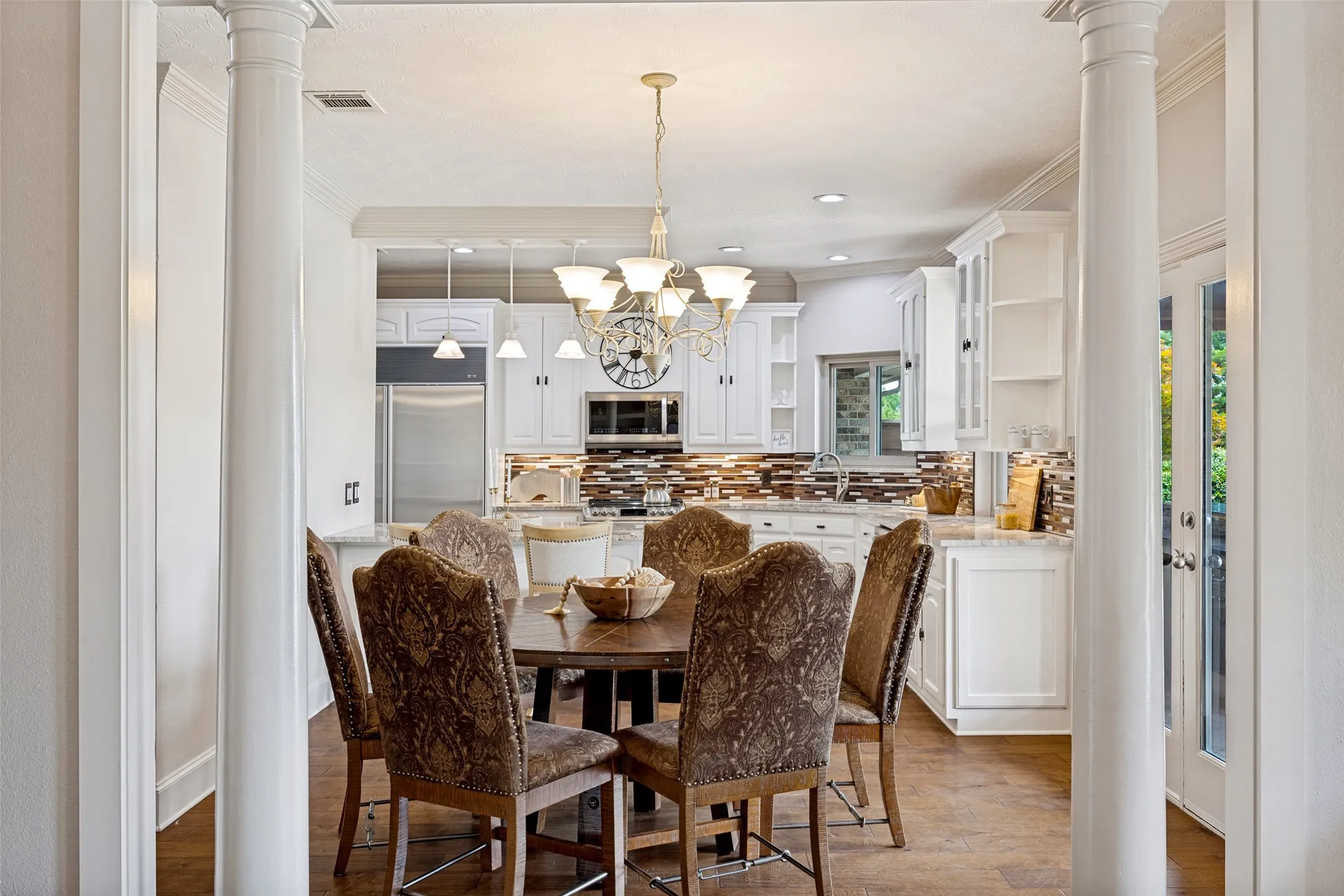 Open-concept dining area featuring wood-finish flooring, a chandelier, and decorative columns