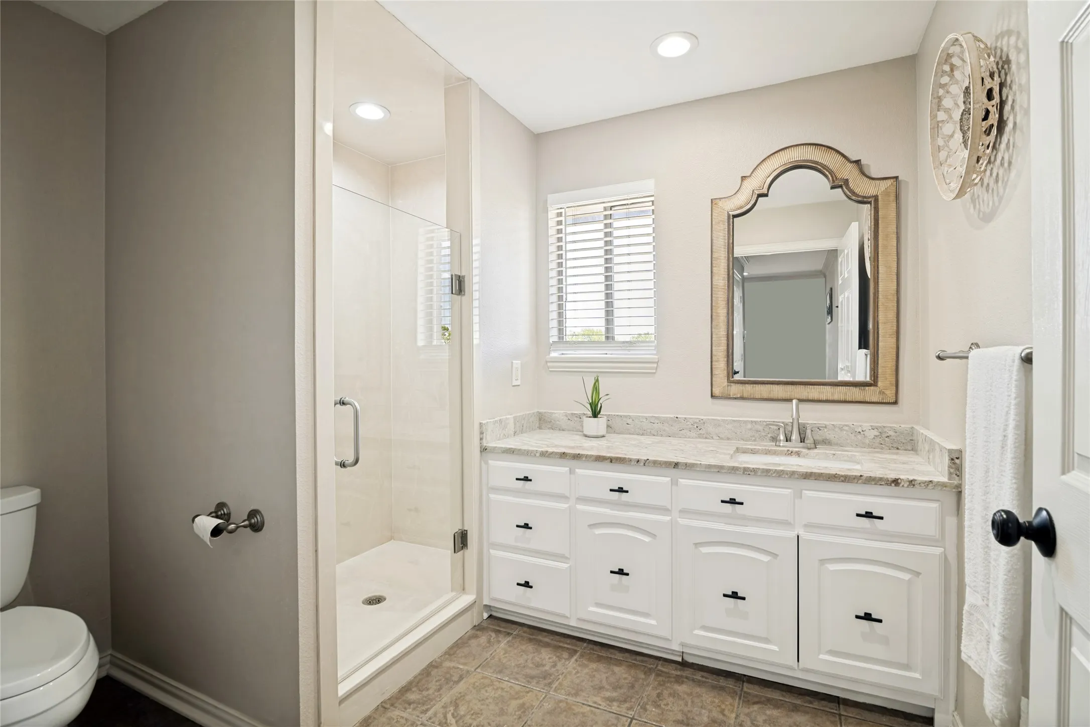 Spa-inspired primary bathroom showcasing a white cabinetry vanity with marble-look countertop, brushed nickel hardware, and integrated sink