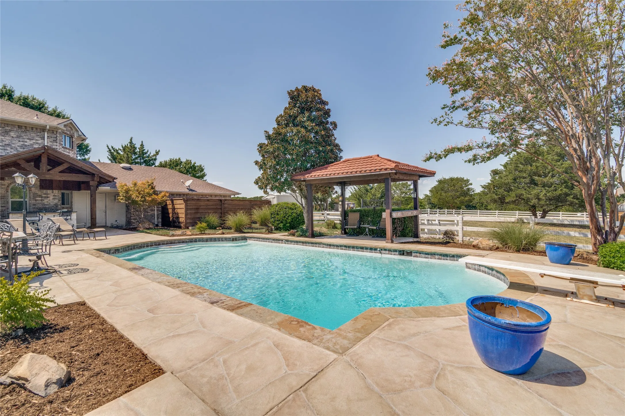 Swimming pool with stone coping and stamped concrete decking, shaded by a gazebo with a tiled roof