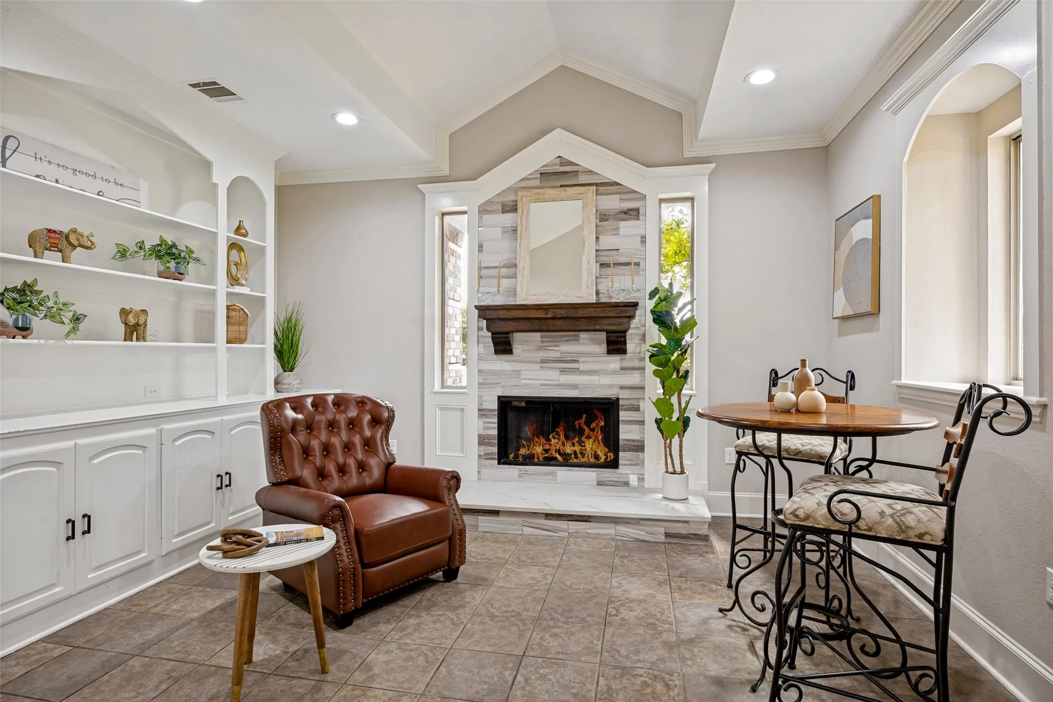 Featuring a fireplace with stacked stone surround and wood mantel, built-in shelving with lower cabinetry, recessed lighting, and tile flooring