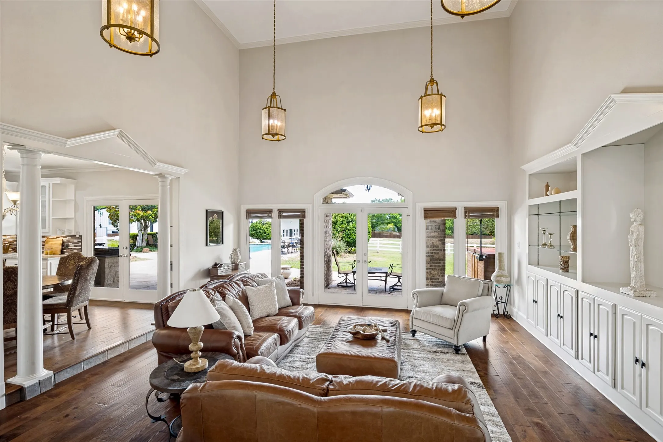Vaulted ceilings enhance this open concept living space featuring wood-finish flooring, custom built-in cabinetry, and multiple sets of French doors leading to exterior areas