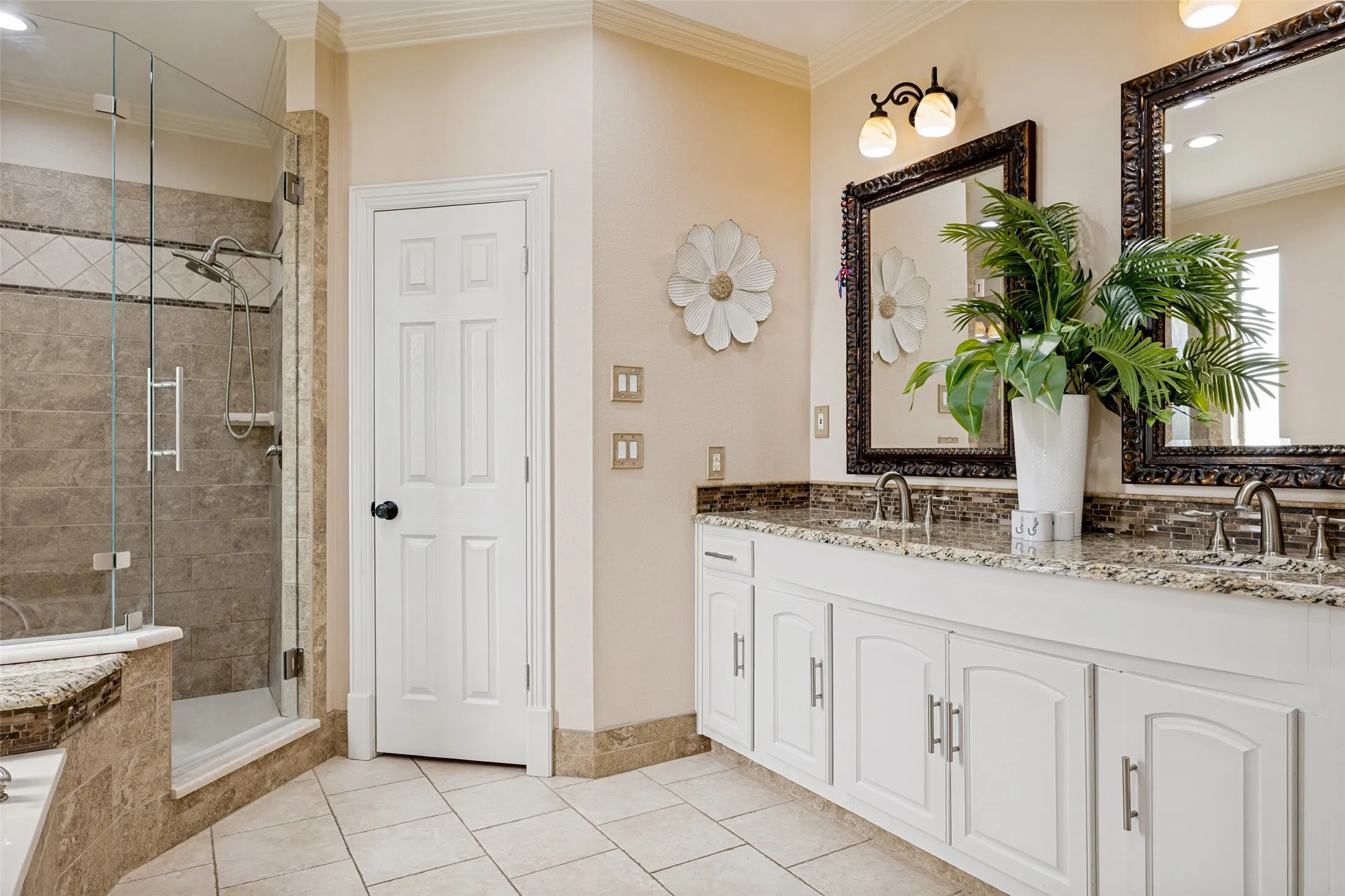 Bathroom featuring a dual vanity with granite countertops, mosaic tile backsplash, and ornate framed mirrors
