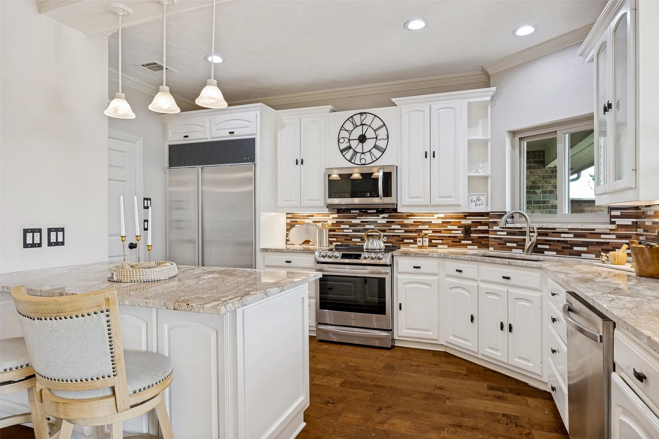 Kitchen featuring white cabinetry, stainless steel appliances and built in Sub Zero refrigerator, granite countertops, wood-finish flooring, and a mosaic tile backsplash, Built in Sub Zero refrigerator