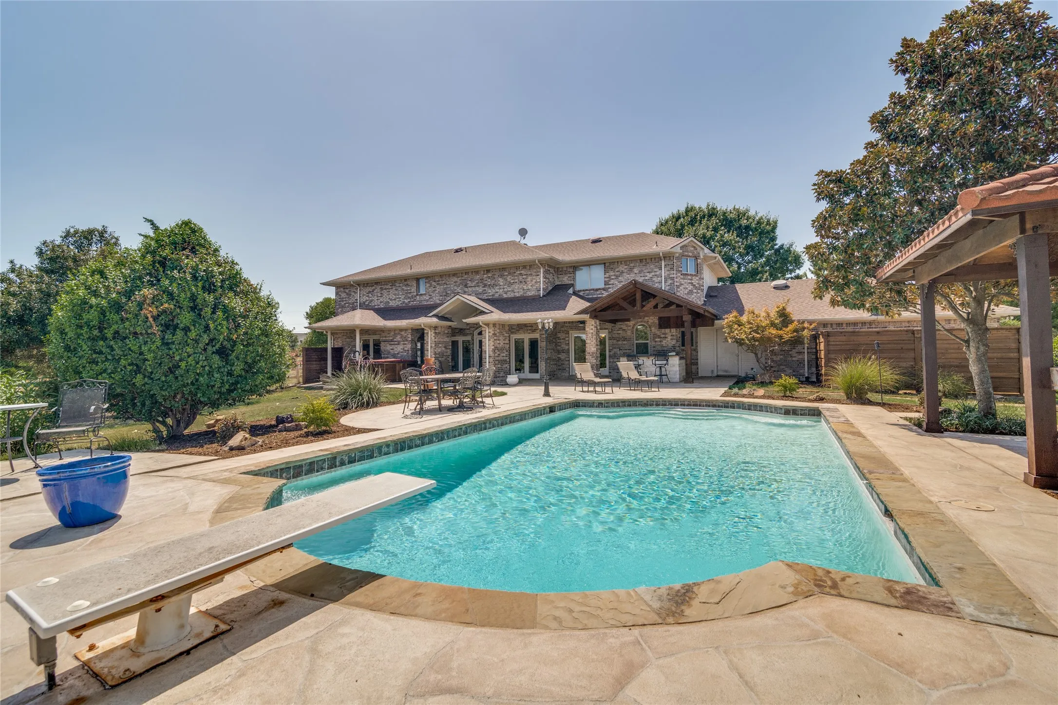 Large backyard featuring an in-ground swimming pool with a diving board, natural stone coping, and expansive concrete decking