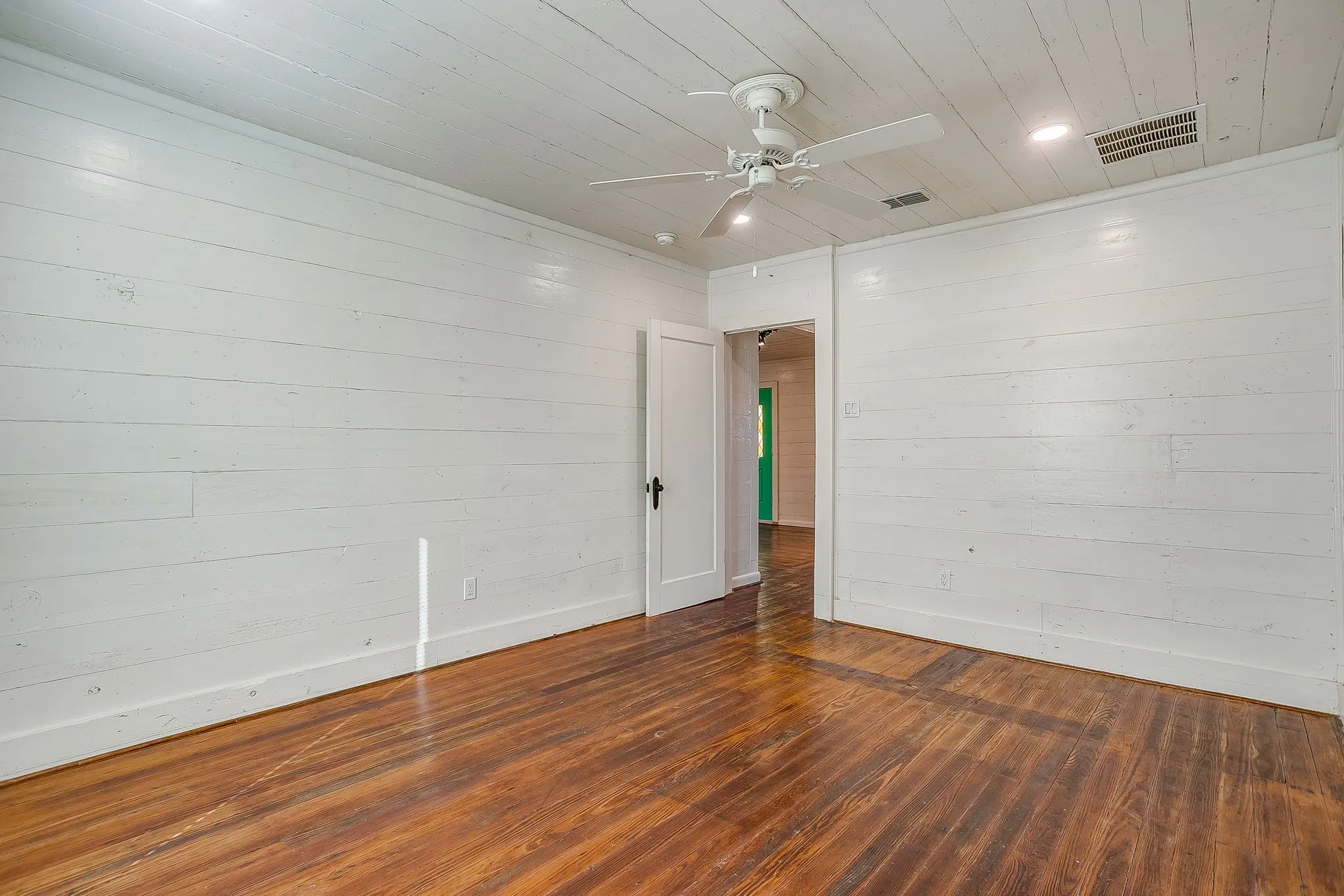 Empty room with wood ceiling, wooden walls, dark wood-style flooring, and ceiling fan