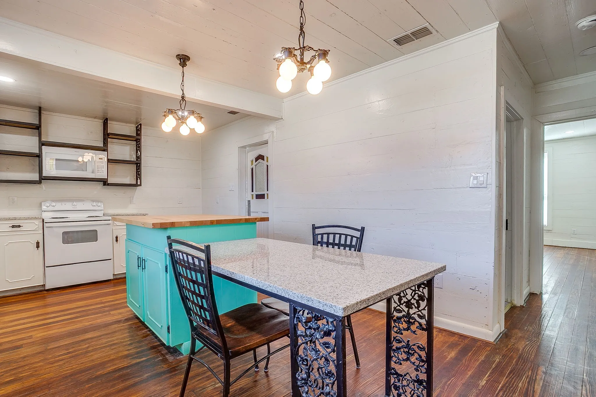 Kitchen with a breakfast bar area, blue cabinets, pendant lighting, wood counters, and white appliances