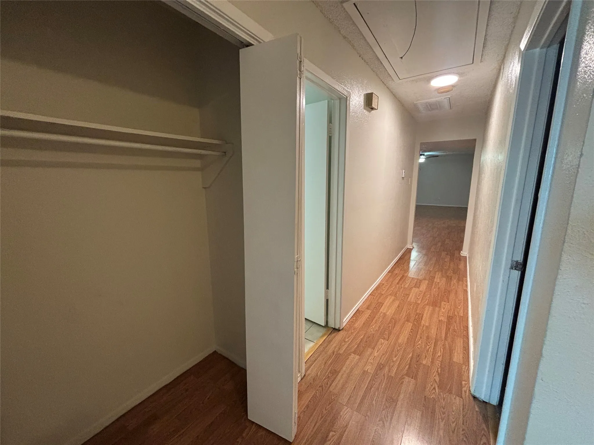Hallway featuring wood-finish flooring, light neutral wall paint, and a built-in closet with shelving