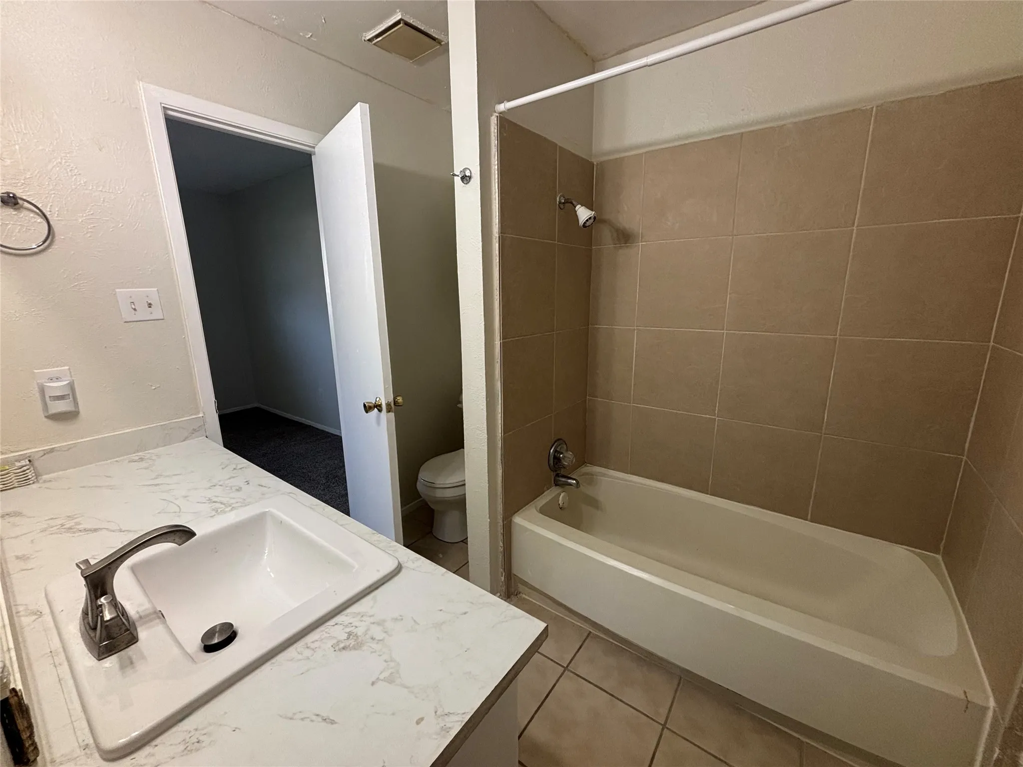 Bathroom featuring a white vanity with a patterned countertop, an integrated rectangular sink with a brushed nickel faucet, a white bathtub, and tan tile shower surround