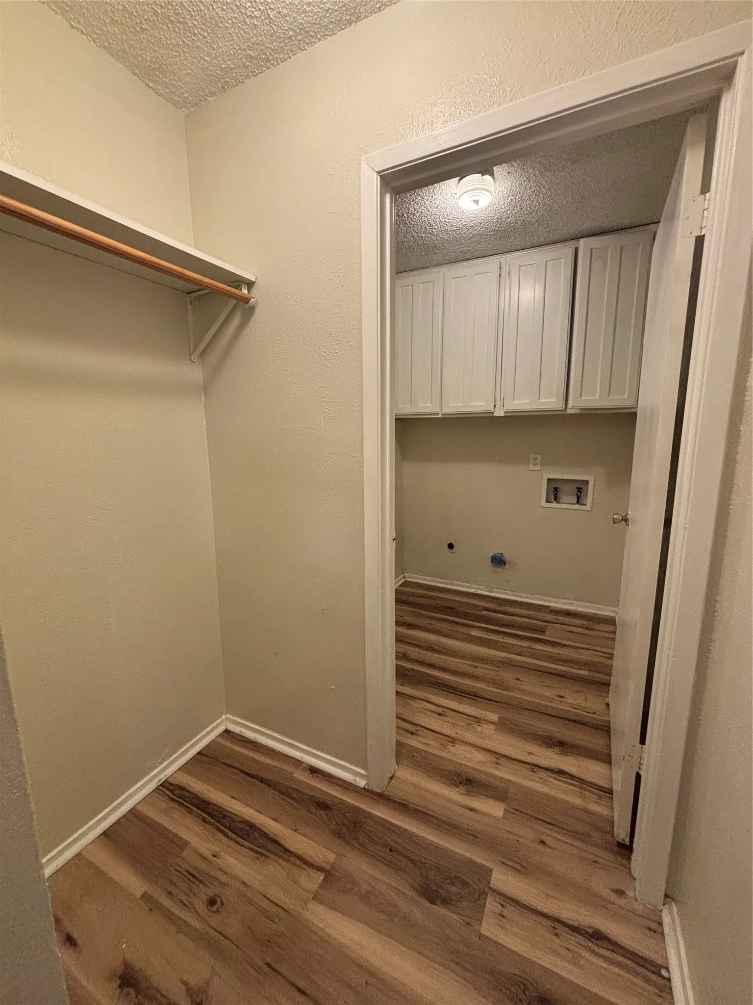 Wood-finish flooring throughout, leading to a utility space with white shaker cabinetry and a ceiling-mounted light fixture