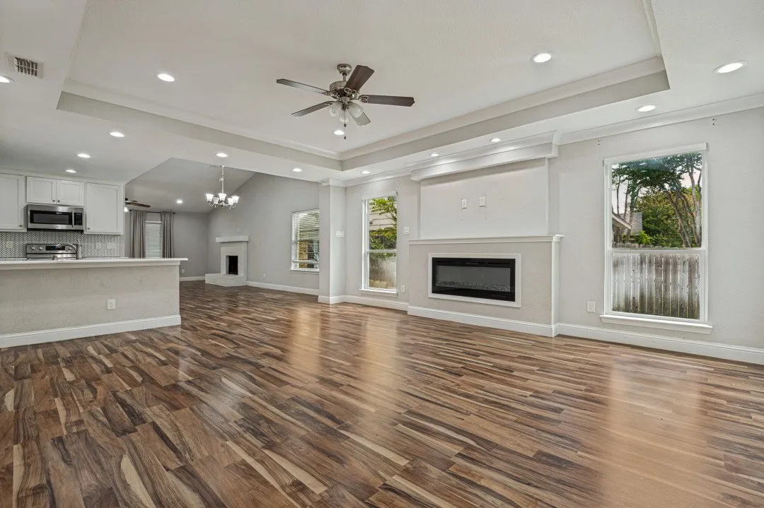 Expansive living area featuring wood-finish flooring, a contemporary linear electric fireplace, and a tray ceiling with recessed lighting