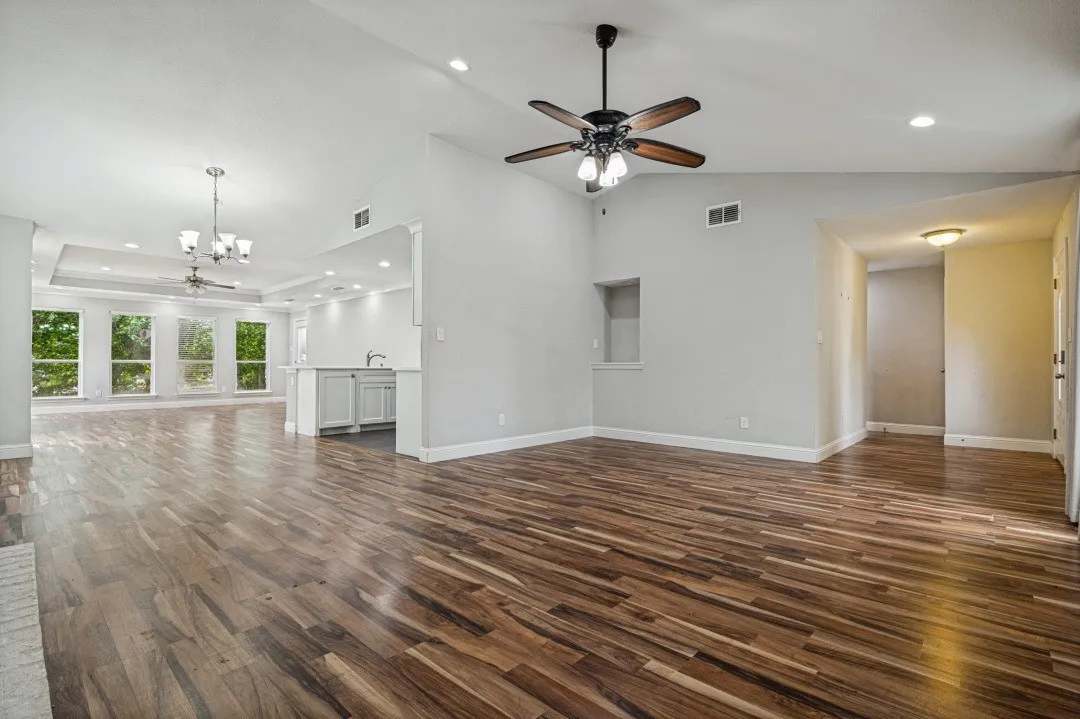 Spacious living area featuring wood-finish flooring, vaulted ceilings, and a decorative ceiling fan