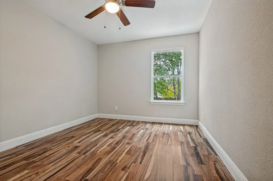 Bedroom featuring wood-finish flooring, a window with exterior tree scenery, a ceiling fan with integrated lighting, and neutral-toned textured walls