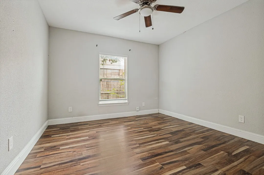 Spacious room featuring wood-finish flooring, light-toned walls, a window with blinds, and a ceiling fan
