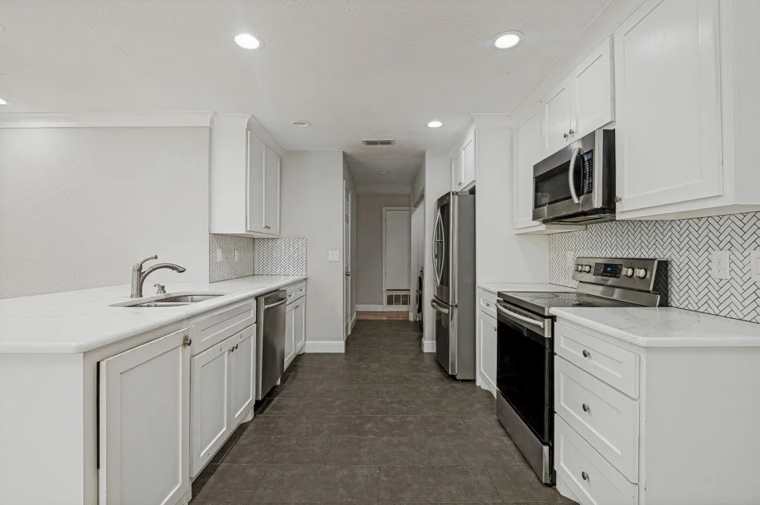 Modern kitchen featuring white shaker cabinetry, stainless steel appliances, herringbone tile backsplash, light-toned countertops, and recessed lighting