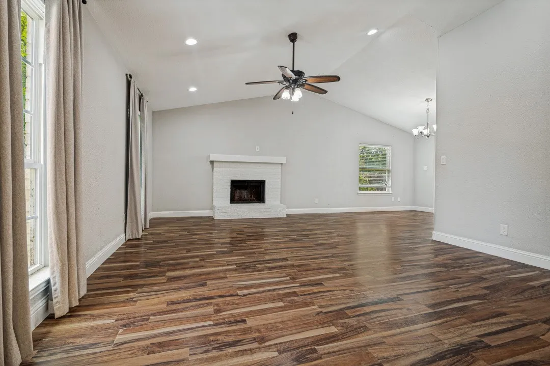 Spacious living area featuring wood-finish flooring, a white brick fireplace, a vaulted ceiling, and recessed lighting