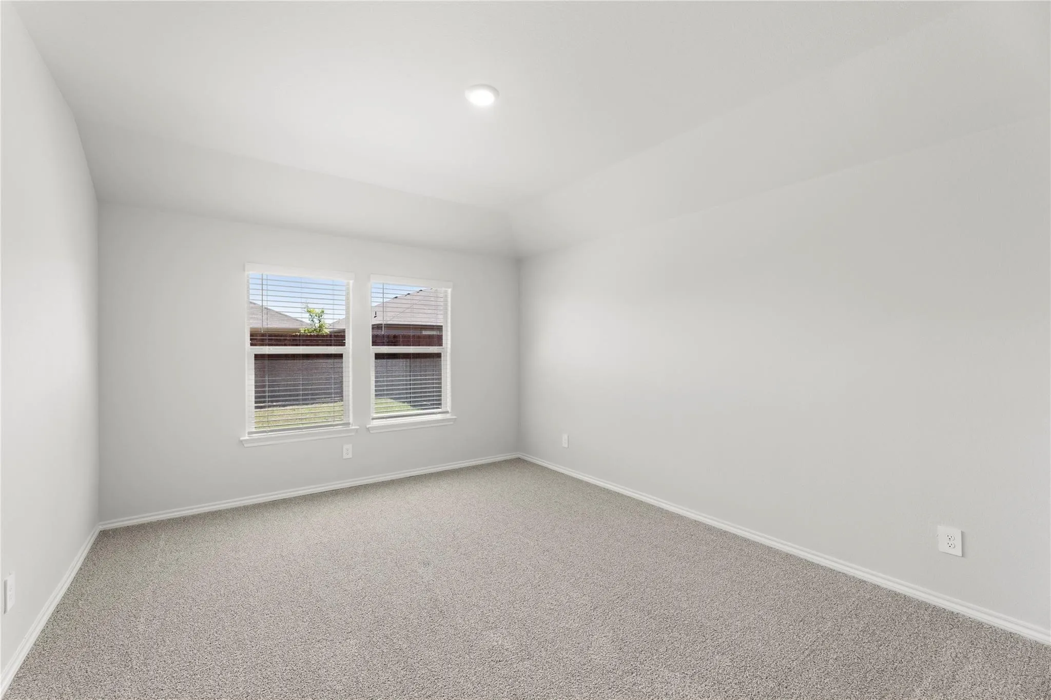 Spacious room featuring neutral carpeting, light gray walls, and two large windows with blinds