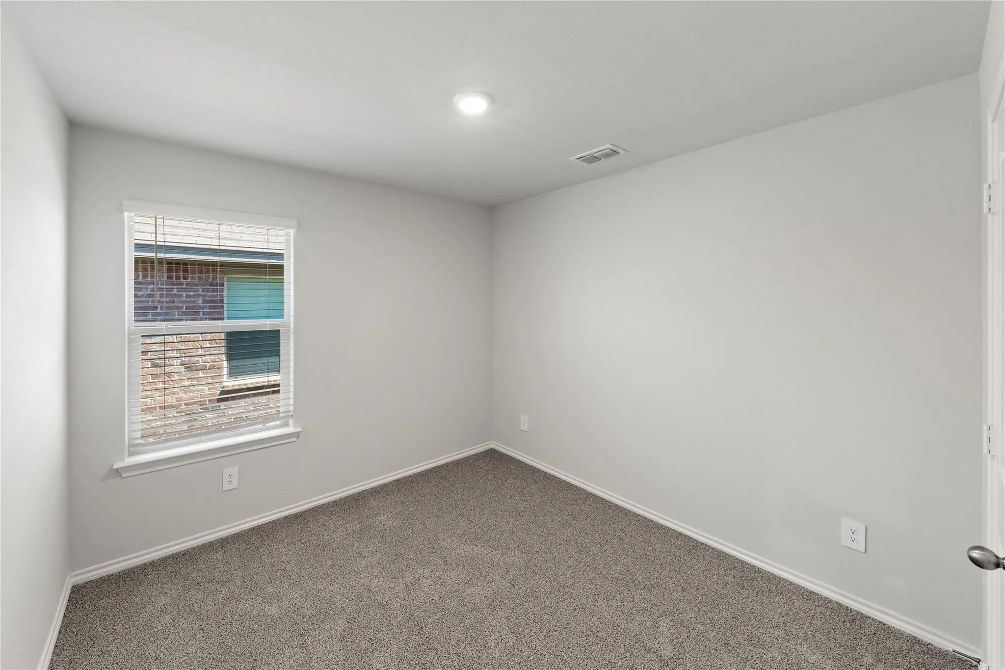Neutral-toned room featuring a single window with blinds, recessed ceiling light, and light gray carpet