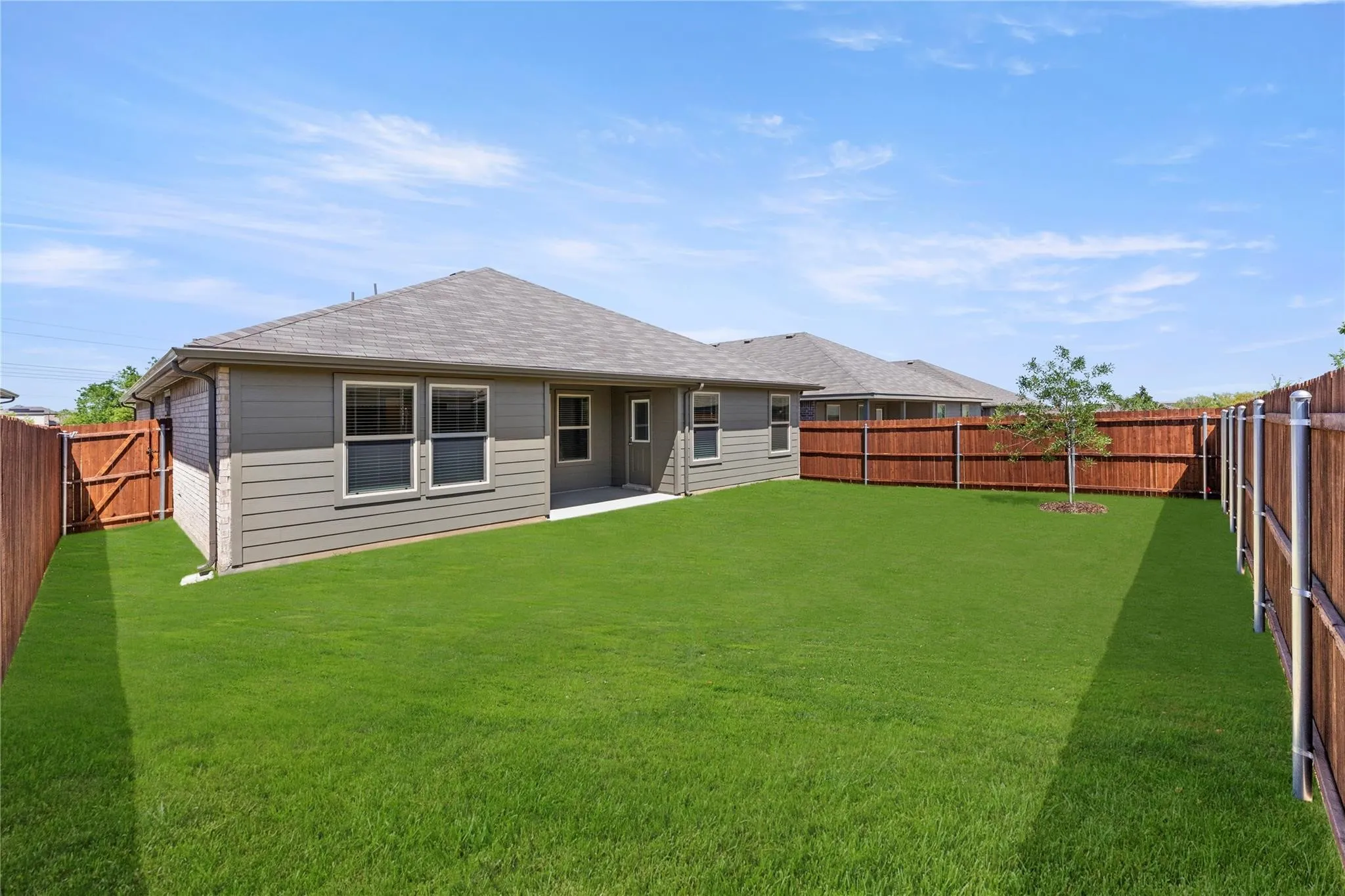 Expansive backyard featuring a manicured lawn, full privacy fencing, and a small tree