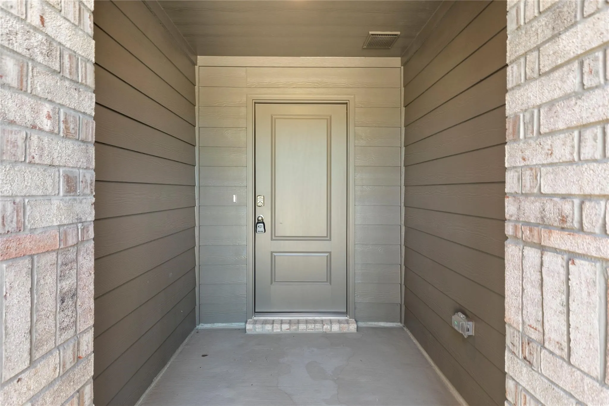 Recessed entryway featuring a paneled entry door, light brick accents, horizontal plank siding, concrete flooring, and a tiled threshold