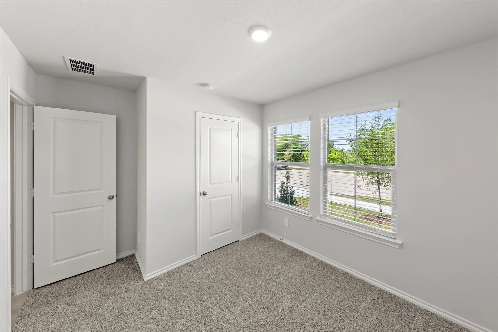 Carpeted room featuring two windows with horizontal blinds, two paneled doors, and a ceiling-mounted light fixture