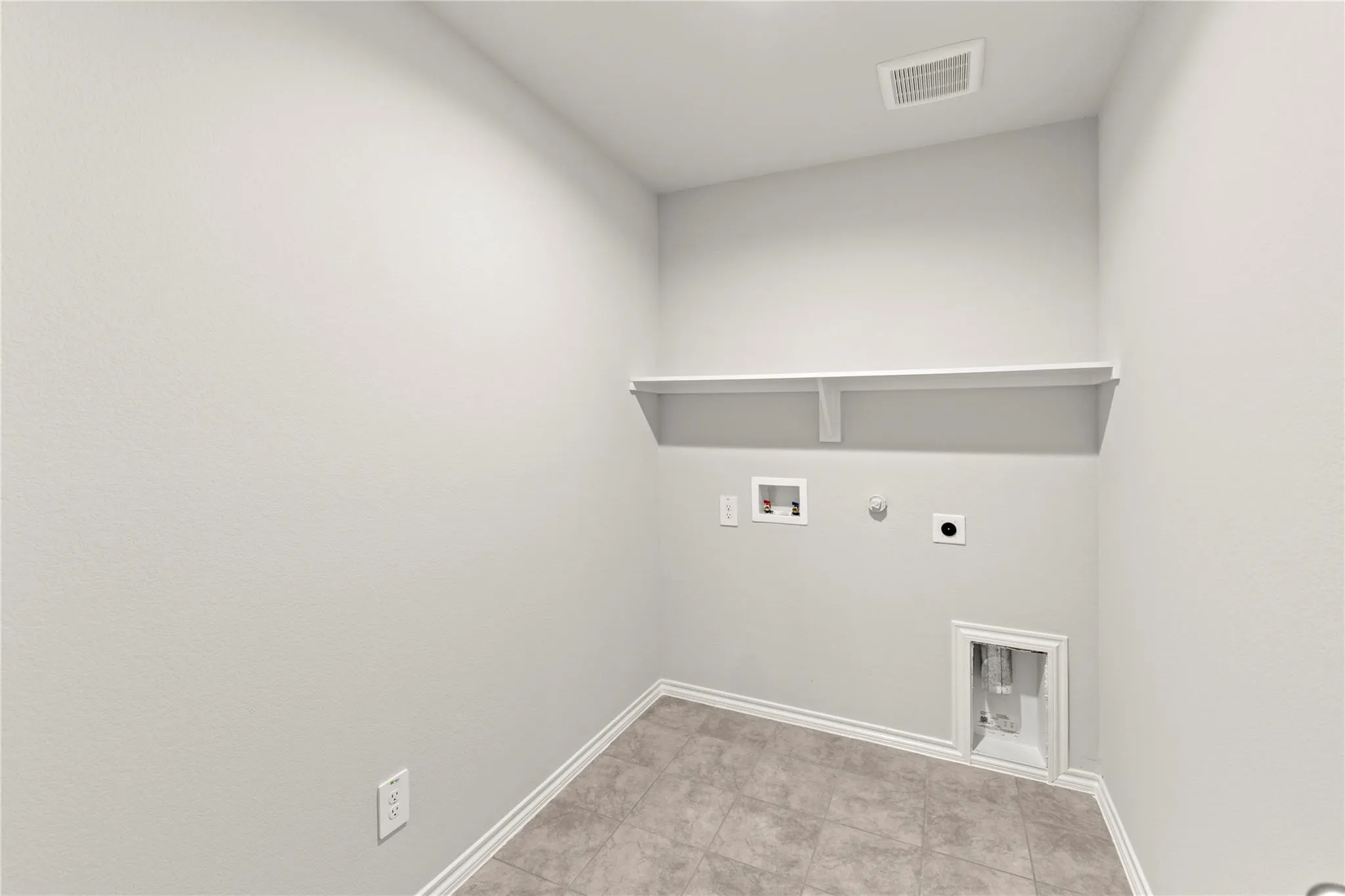 Utility room featuring light-toned tile flooring, a wall-mounted shelf, and standard appliance hookups