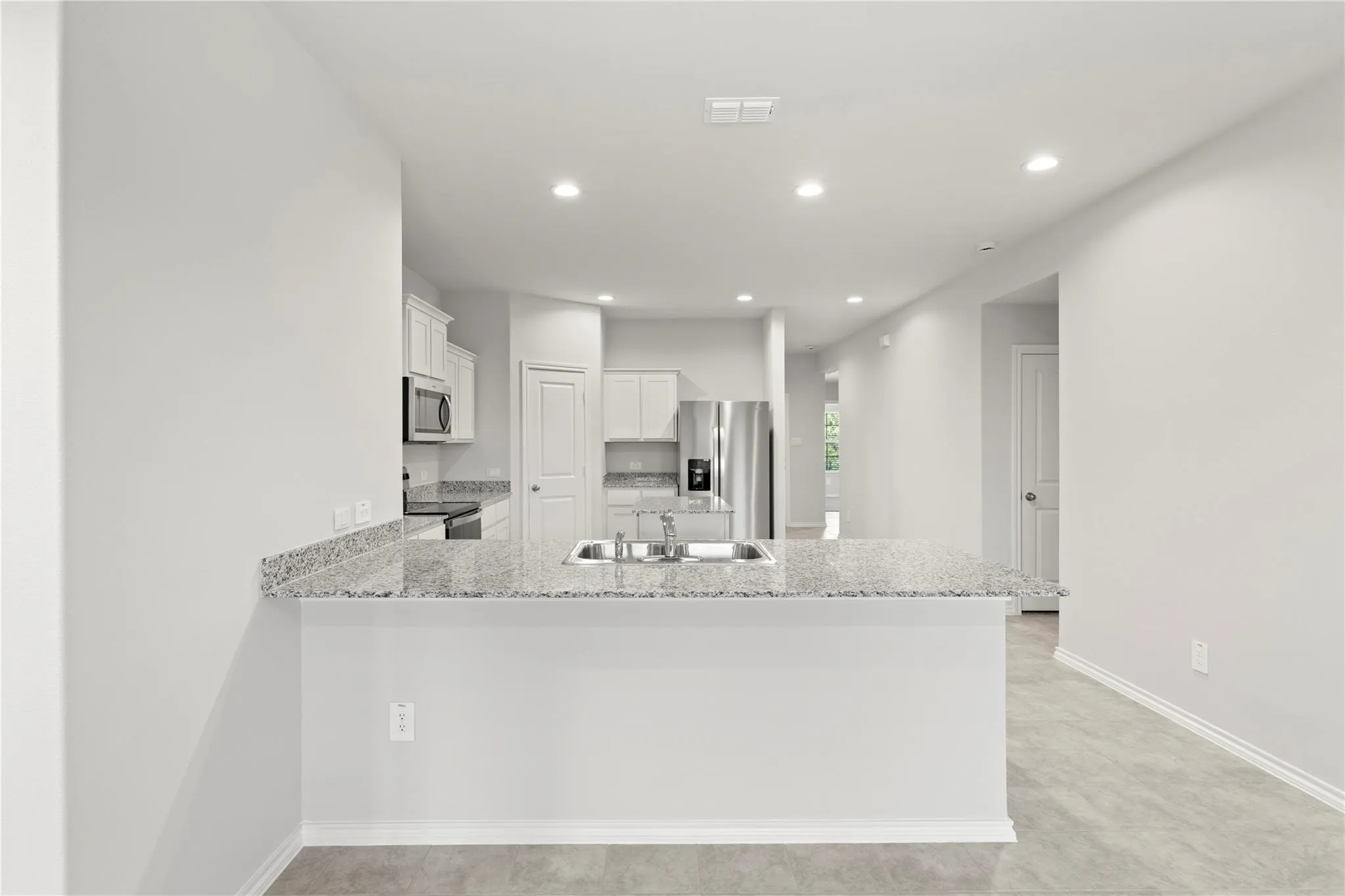 Kitchen featuring a breakfast bar with stone-finish countertop, stainless steel appliances, white cabinetry, recessed lighting, and tile flooring