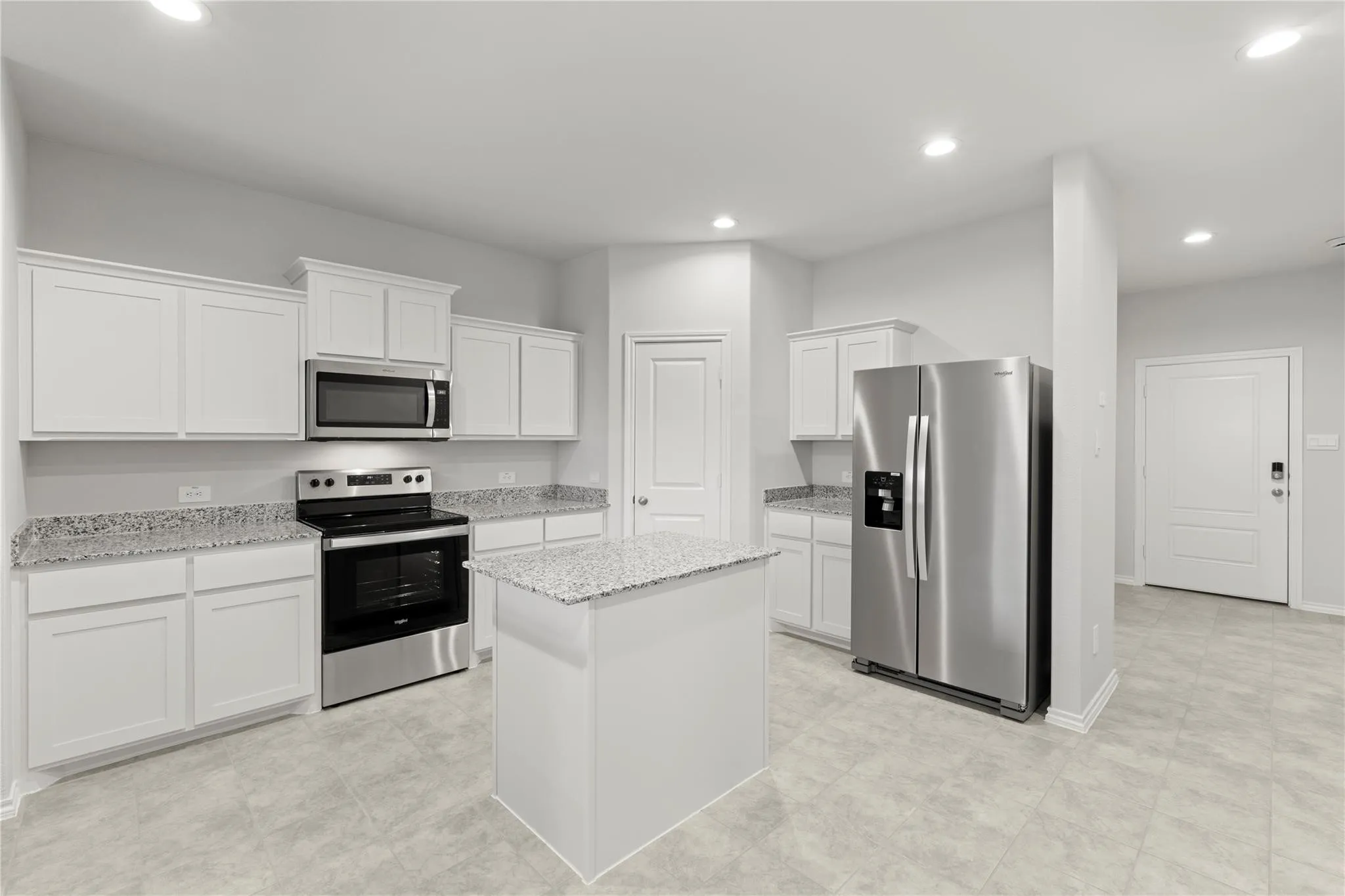 Kitchen featuring white cabinetry, granite countertops, stainless steel appliances including a refrigerator, range, and microwave, and a central island