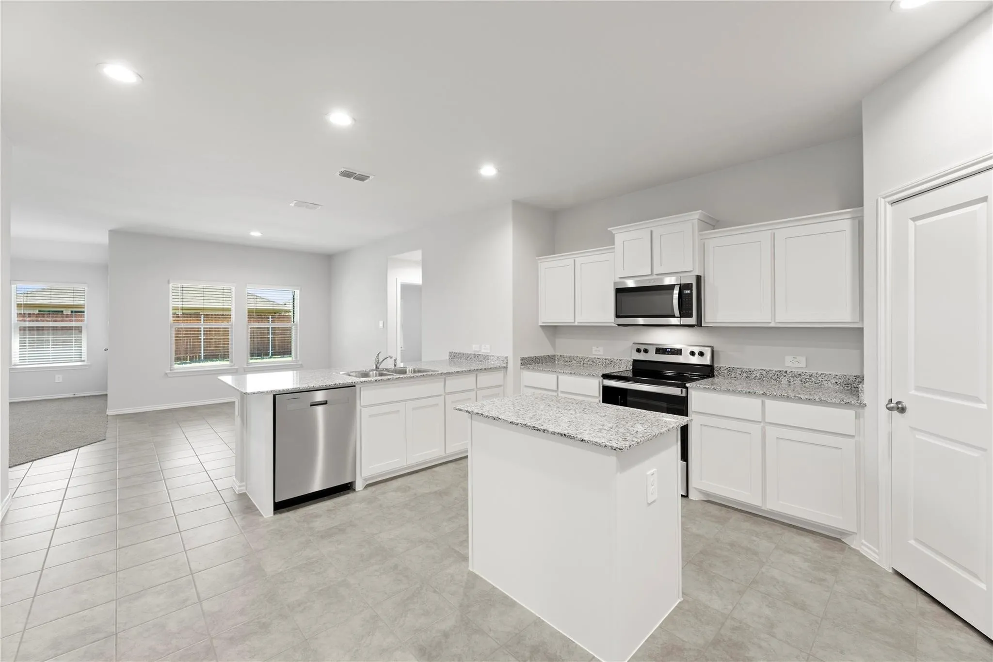 Open-concept kitchen featuring an island, white cabinetry, integrated stainless steel appliances, and light-toned countertops