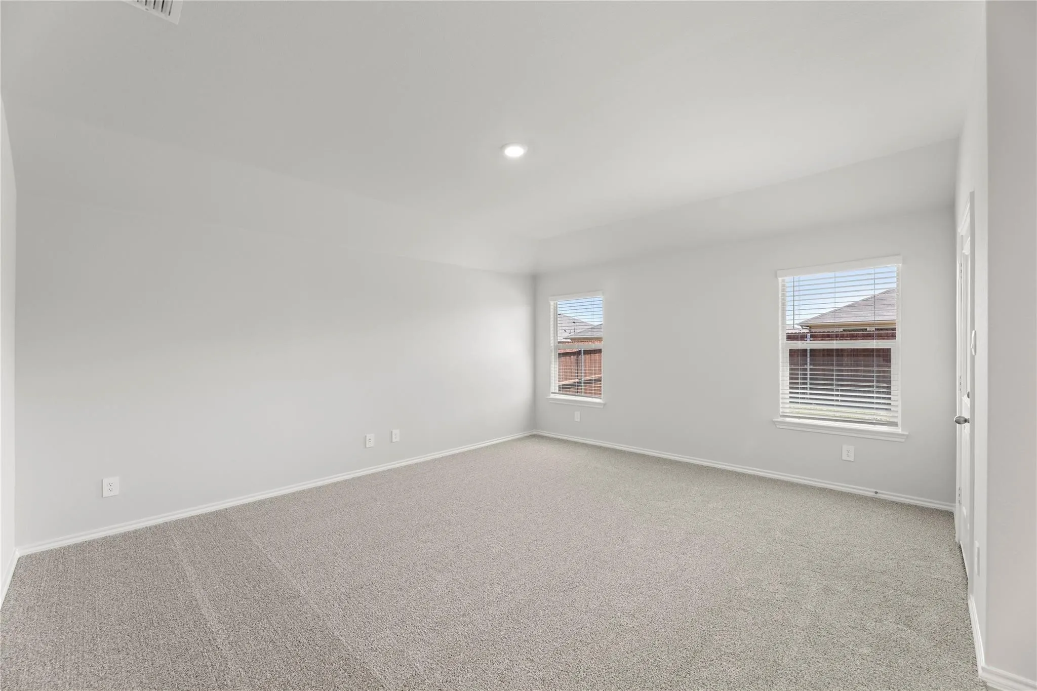 Spacious room with light neutral carpeting, white walls, two windows with blinds, and recessed ceiling lighting